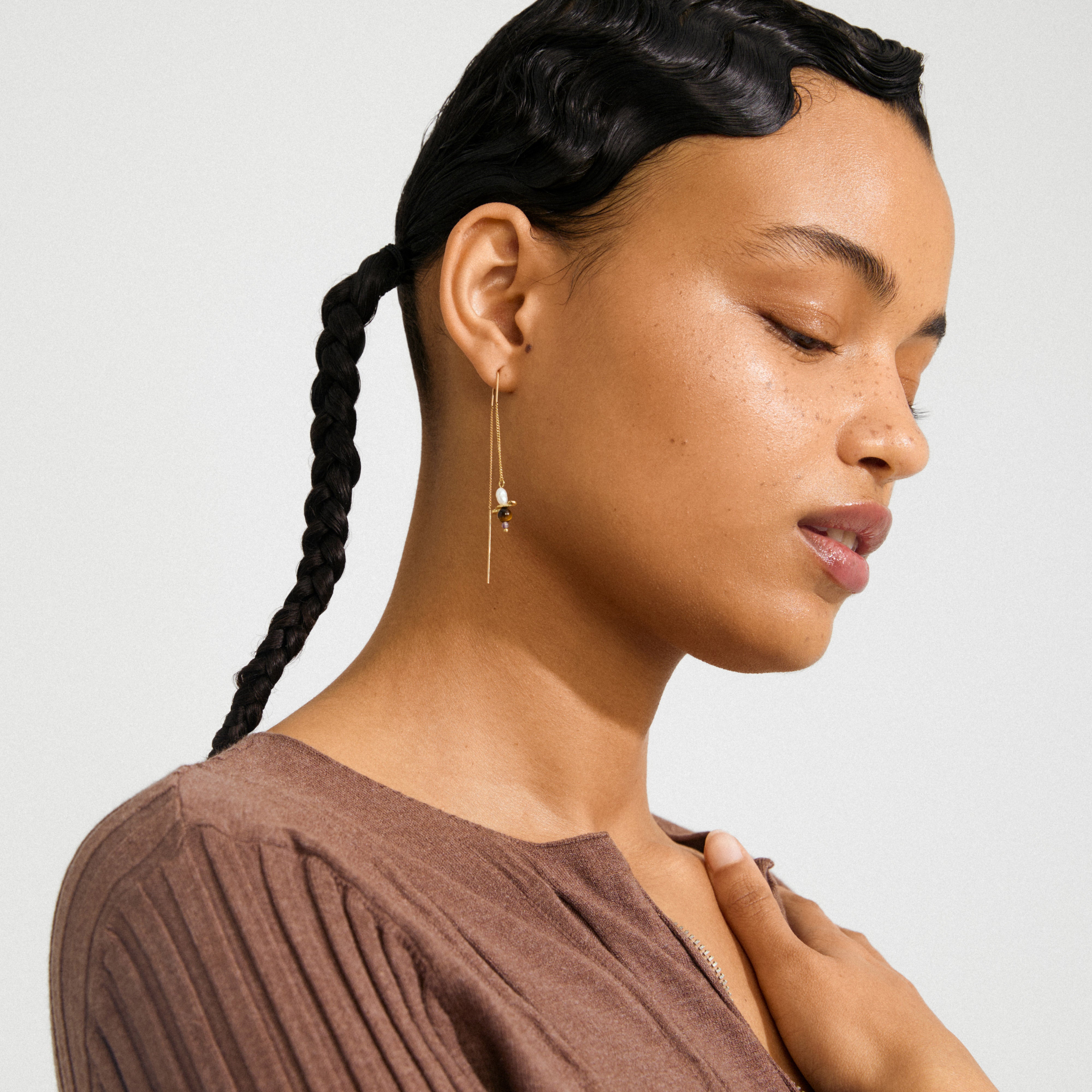 Young person wearing SEQUOIA gold-plated chain earrings with a pearl and dark bead, showcasing a playful, boho style with a rib-knit top.