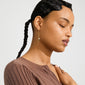 Young person wearing SEQUOIA gold-plated chain earrings with a pearl and dark bead, showcasing a playful, boho style with a rib-knit top.