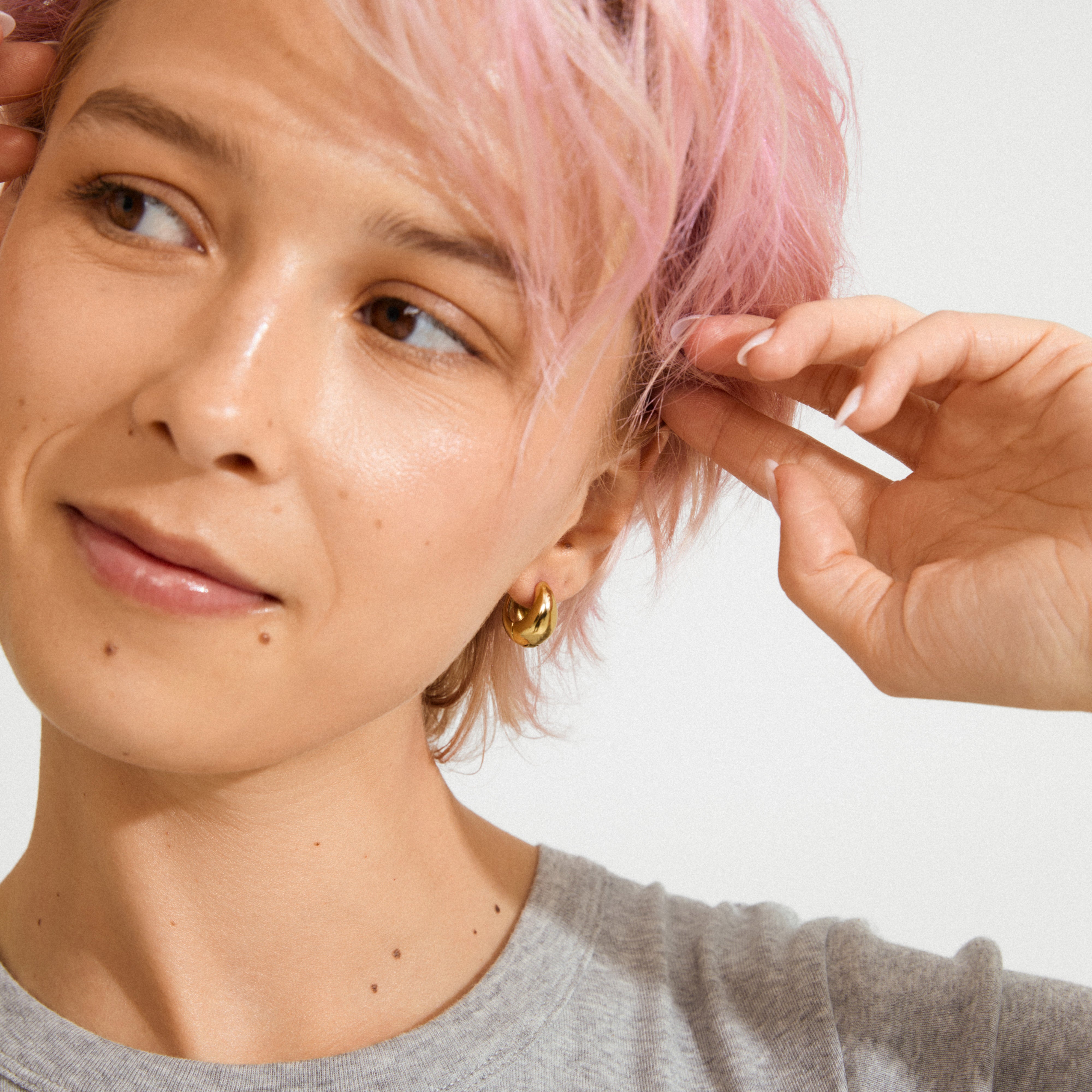 Close-up of a person wearing BRAXTYN gold-plated chunky hoop earrings, showcasing their shiny, bubble dome silhouette against a plain background.