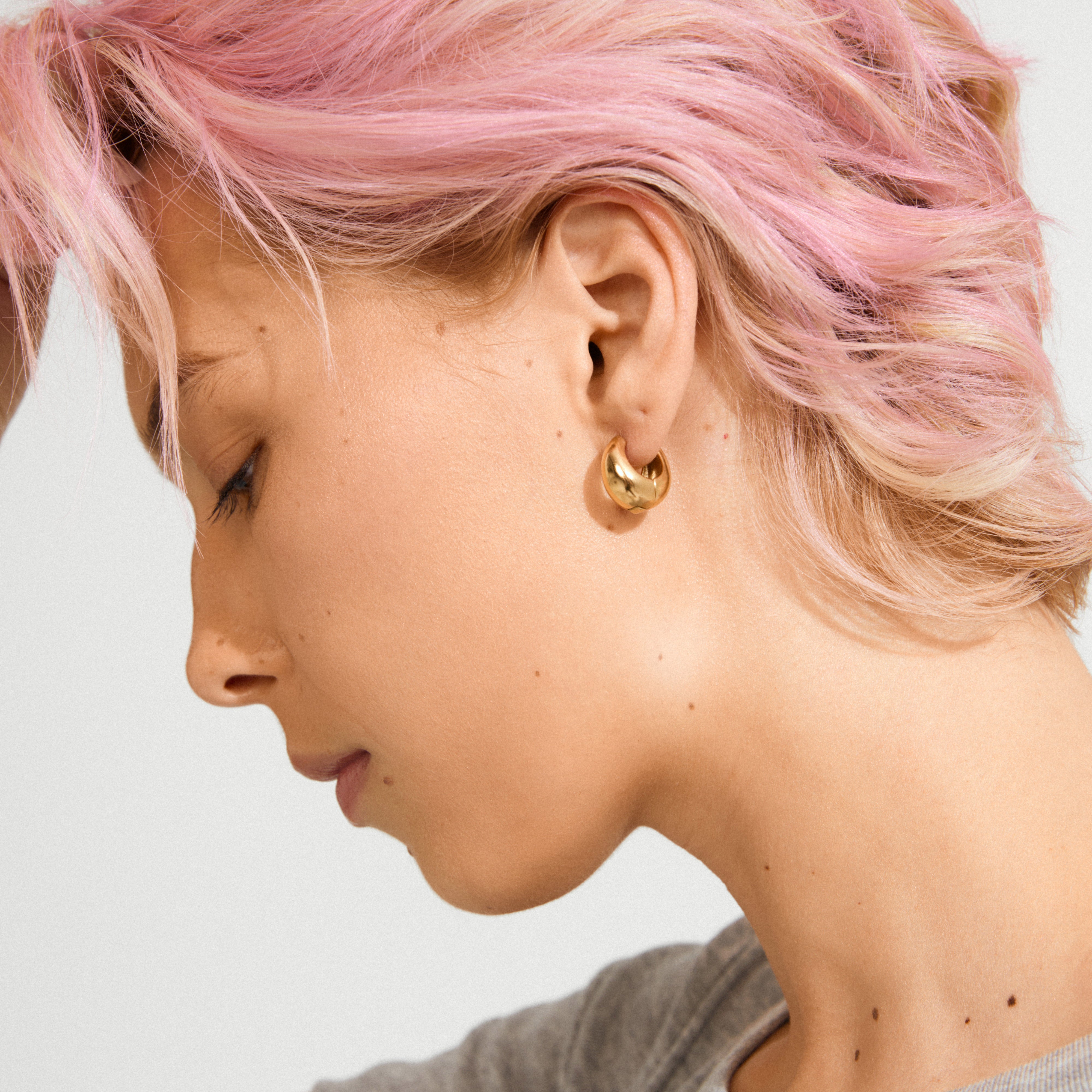Side profile of a person wearing BRAXTYN gold-plated chunky hoop earring by Pilgrim, showcasing its shiny bubble dome silhouette and retro-inspired design.