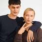 Two young adults showcase the BRAXTYN gold-plated ring, highlighting its chunky, minimalist design against a casual backdrop. The ring adorns a woman's hand in the photo.
