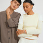Two models showcase the AIKO bracelet gold-plated by Pilgrim, featuring a wavy, organic design on the young man's wrist in a minimalist fashion setting.