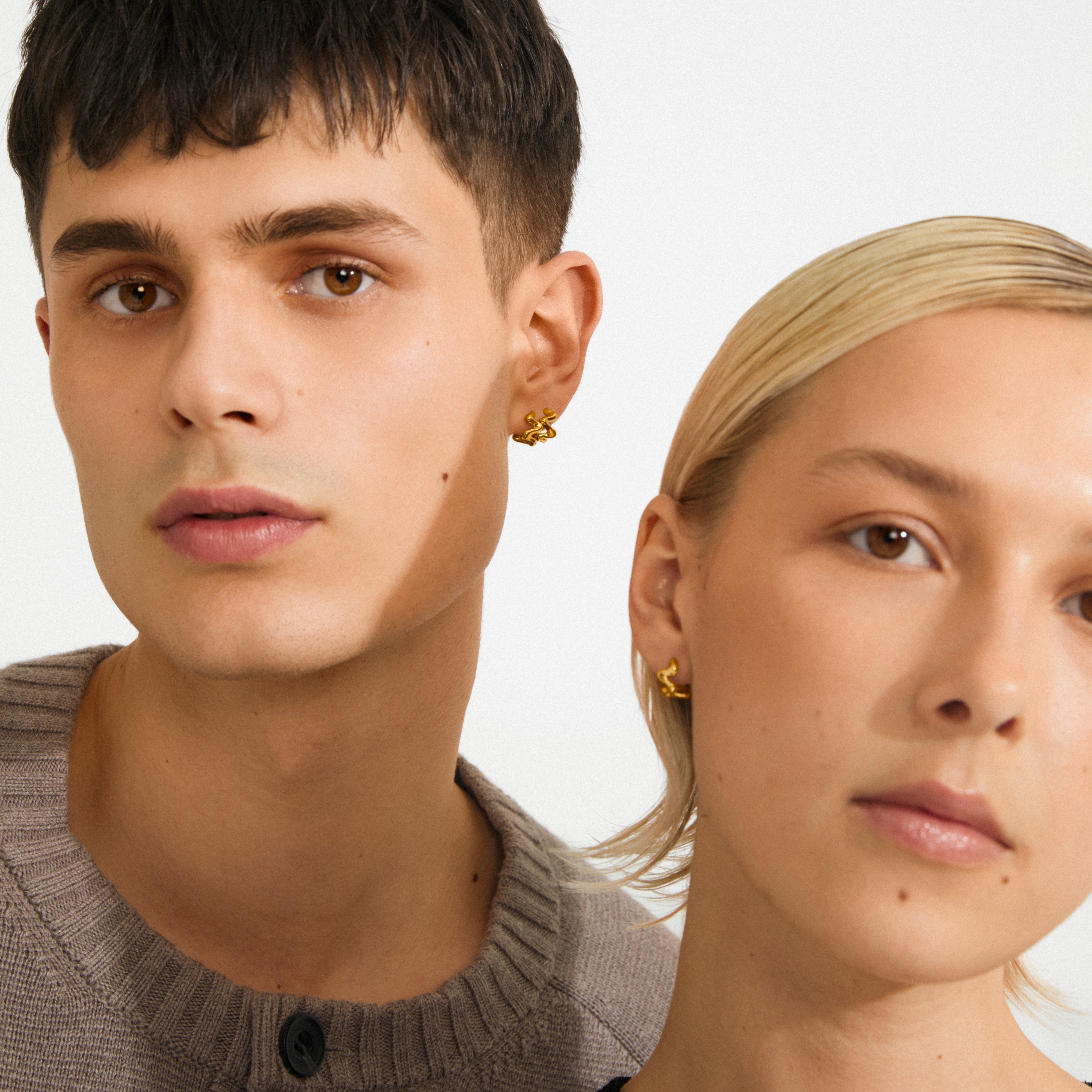 Two young models showcase AIKO earring gold-plated hoops, emphasizing their wavy, sculptural design, epitomizing Pilgrim's blend of timeless elegance and modern style.