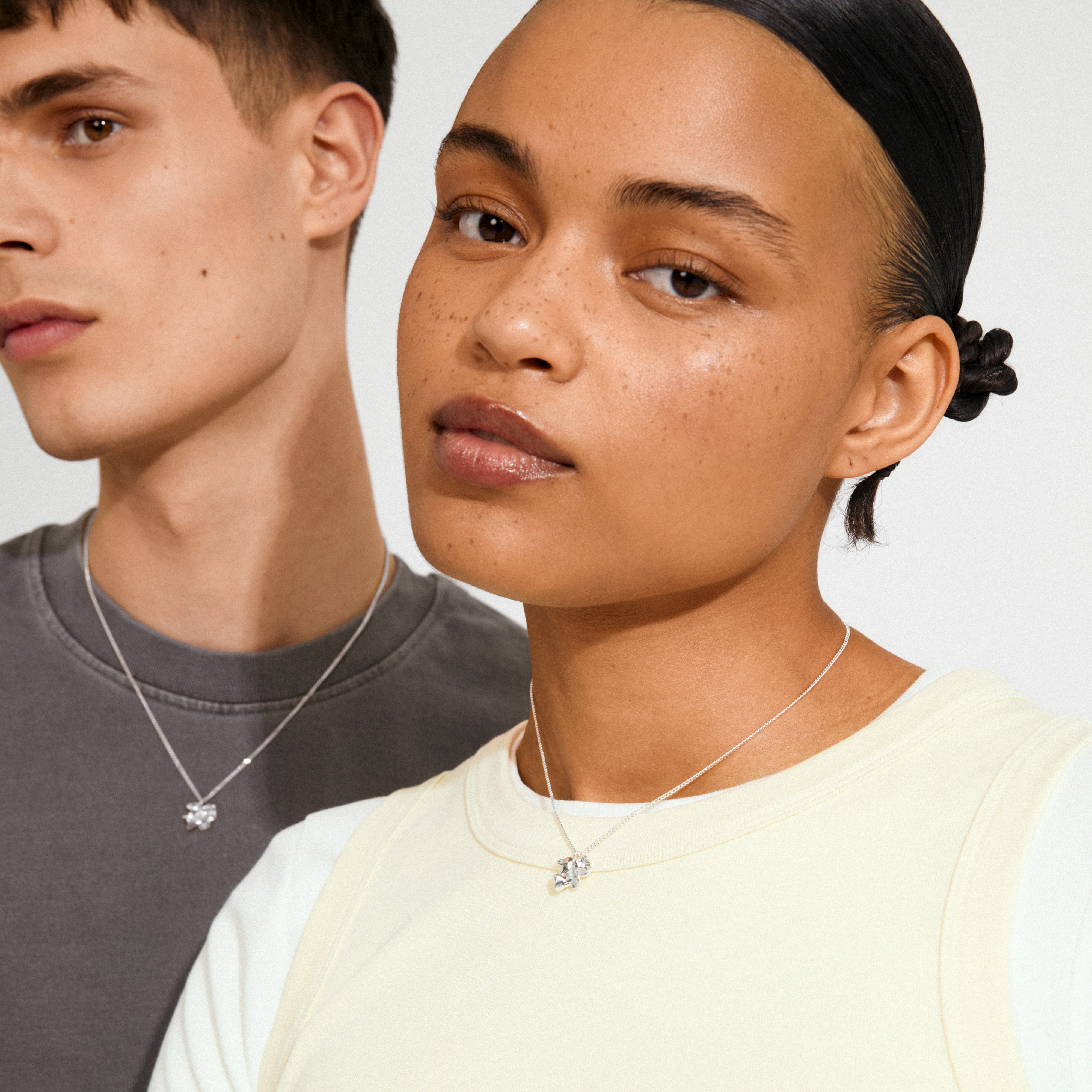 Two young models wear the TIMBER necklace, showcasing its fine silver-plated chain and abstract flower pendant, embodying minimalist style and Scandinavian elegance.