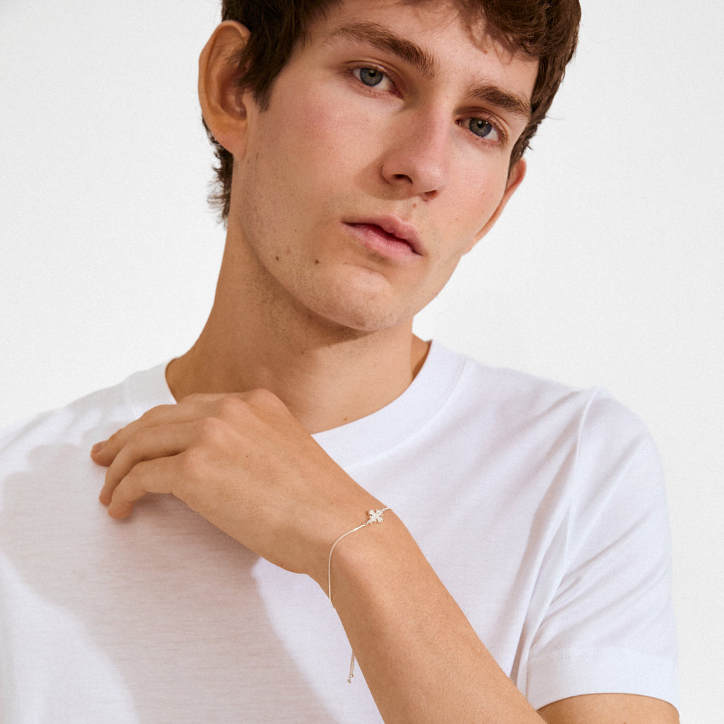 Young man wearing the DAGMAR bracelet silver-plated, featuring a dainty flower charm with sparkling stones, highlighting its classic elegance and historical significance.