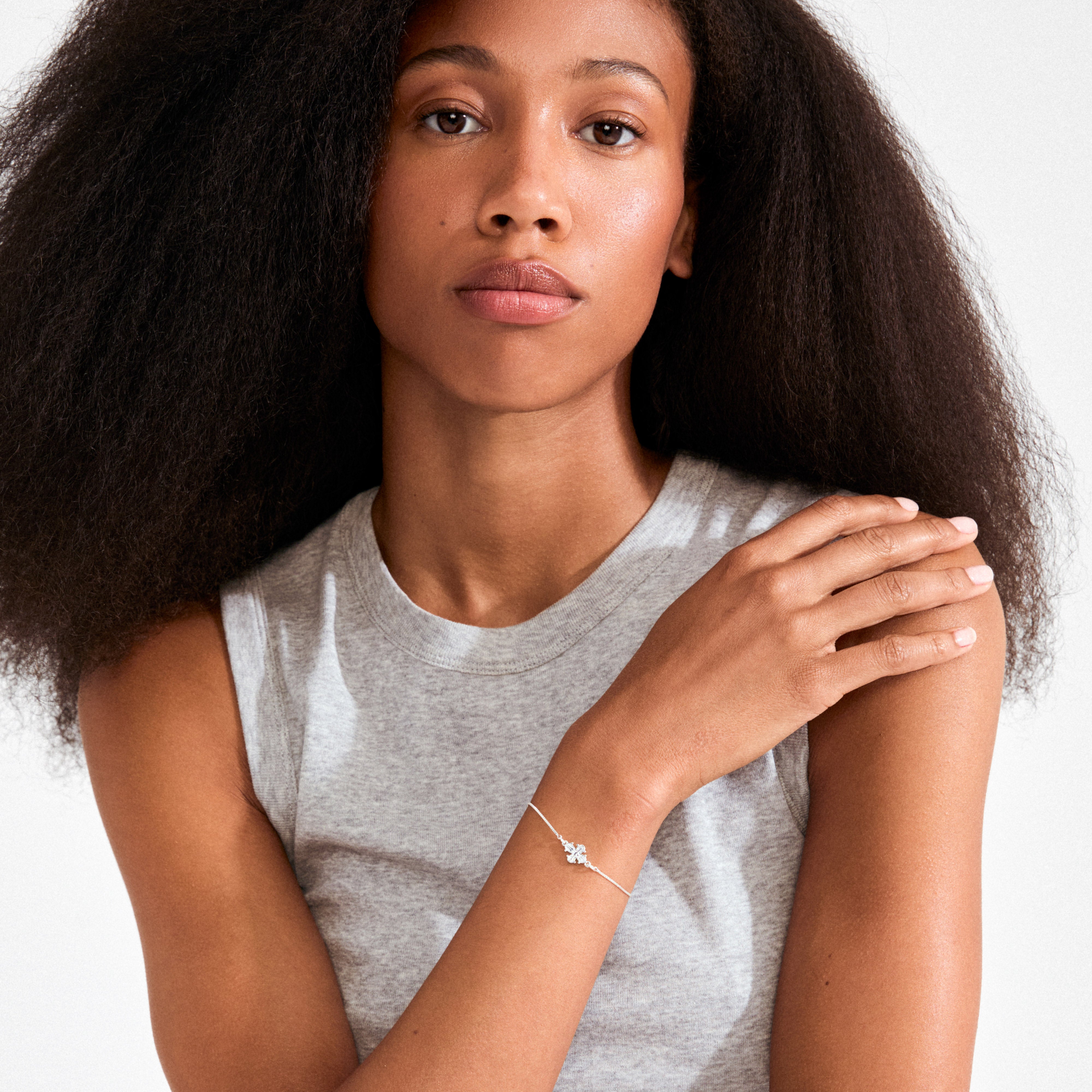 Young woman wearing the DAGMAR bracelet silver-plated by Pilgrim, featuring a delicate silver chain and cross charm, styled simply against a plain background.
