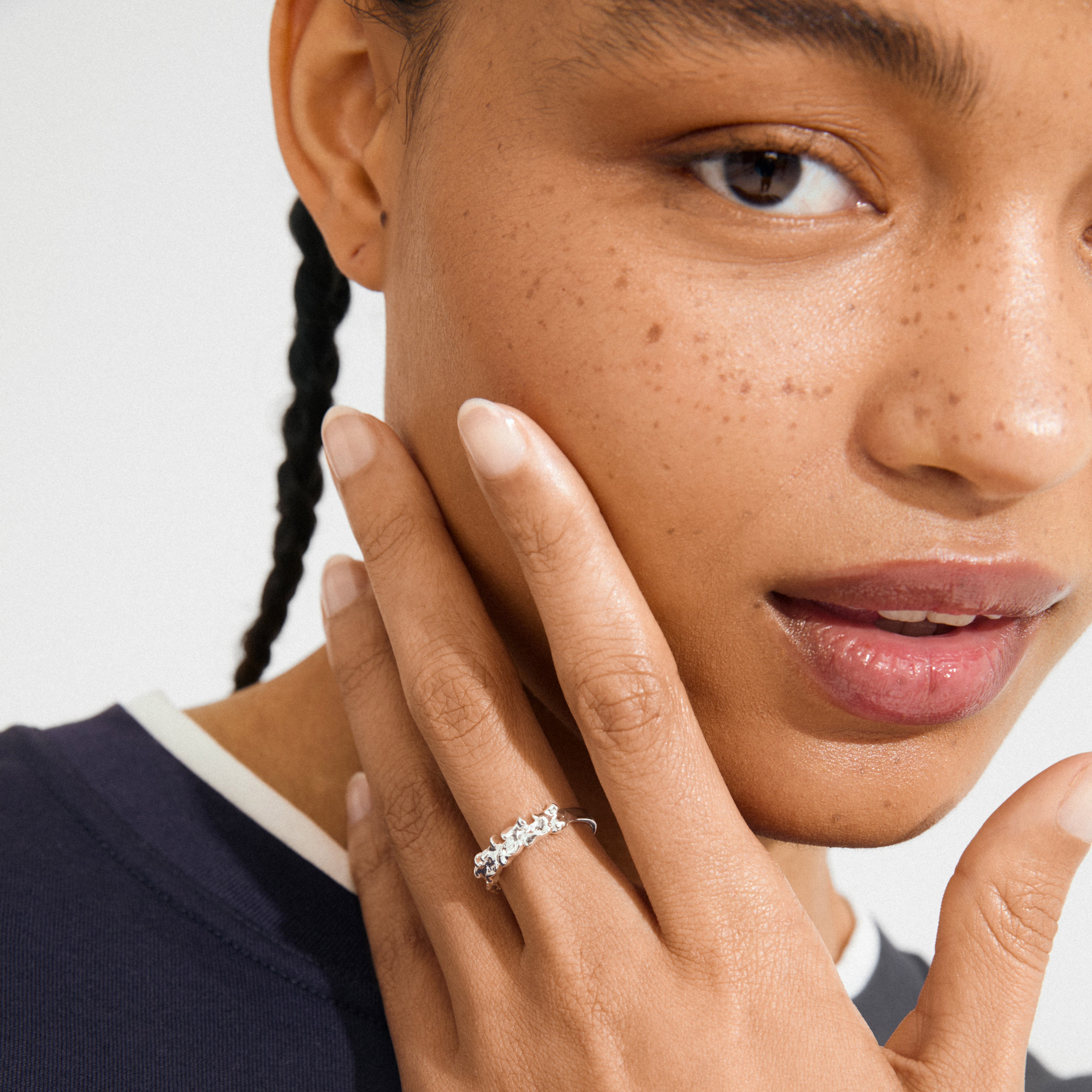 Close-up of a person wearing Pilgrim's silver-plated TIMBER ring, showcasing fine floral details and adjustable fit on the left hand touching their cheek.