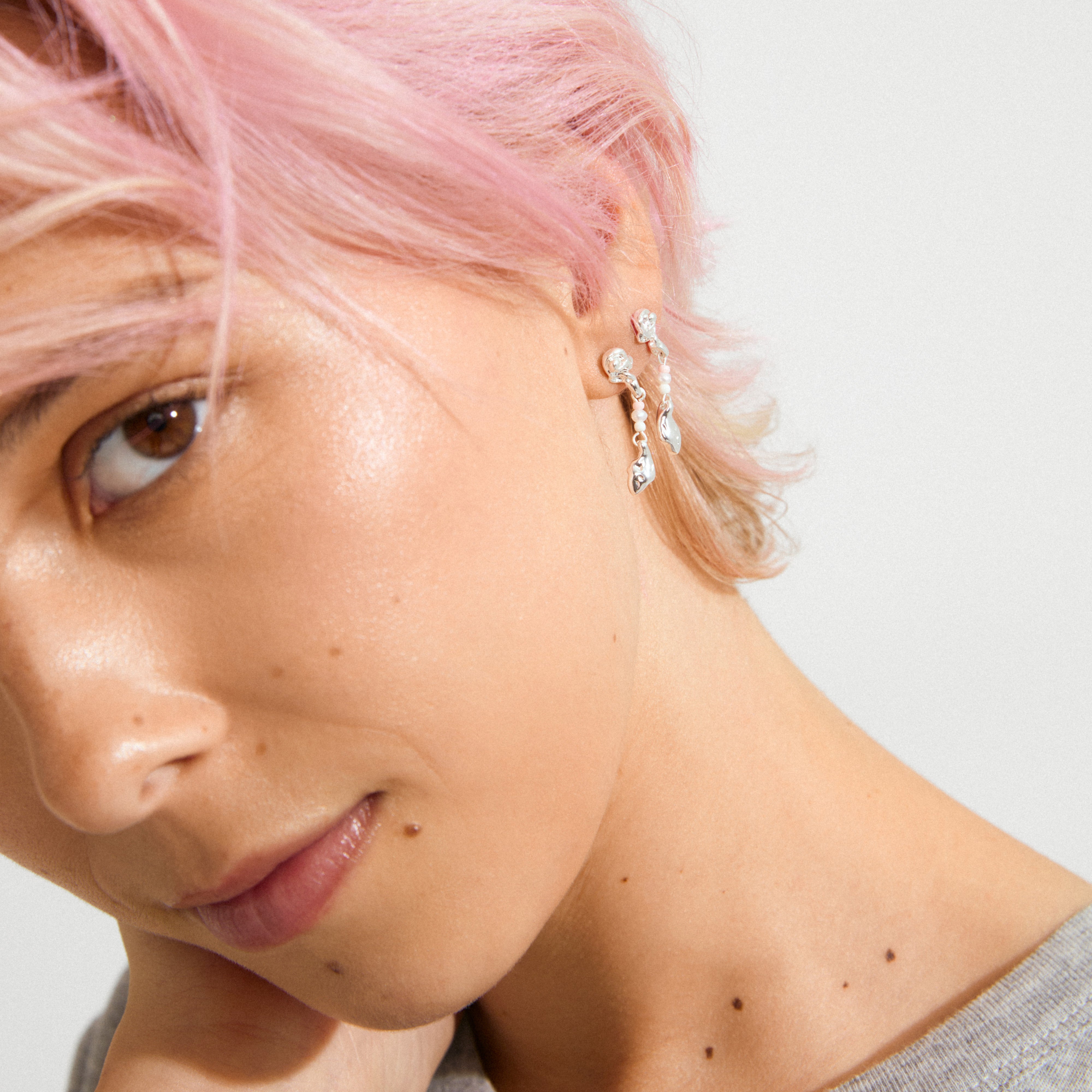 Profile close-up showcasing SEQUOIA earrings silver-plated by Pilgrim, featuring dangling leaf-shaped metal and beads, highlighting modern elegance with a romantic touch.