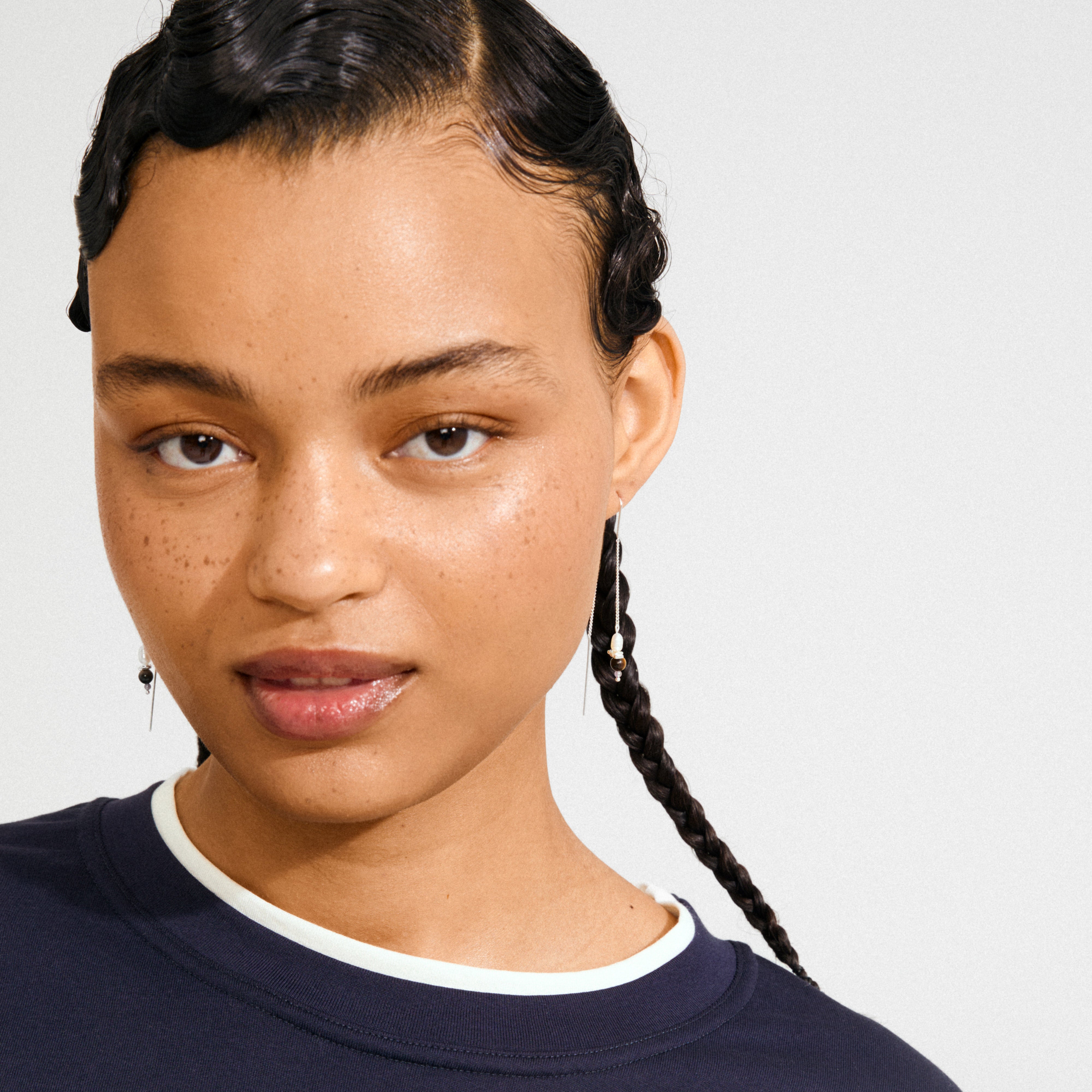Young person wearing SEQUOIA chain earrings silver-plated, featuring delicate chains with organic pendants and tiny pearls, styled with a navy top and braided hair.