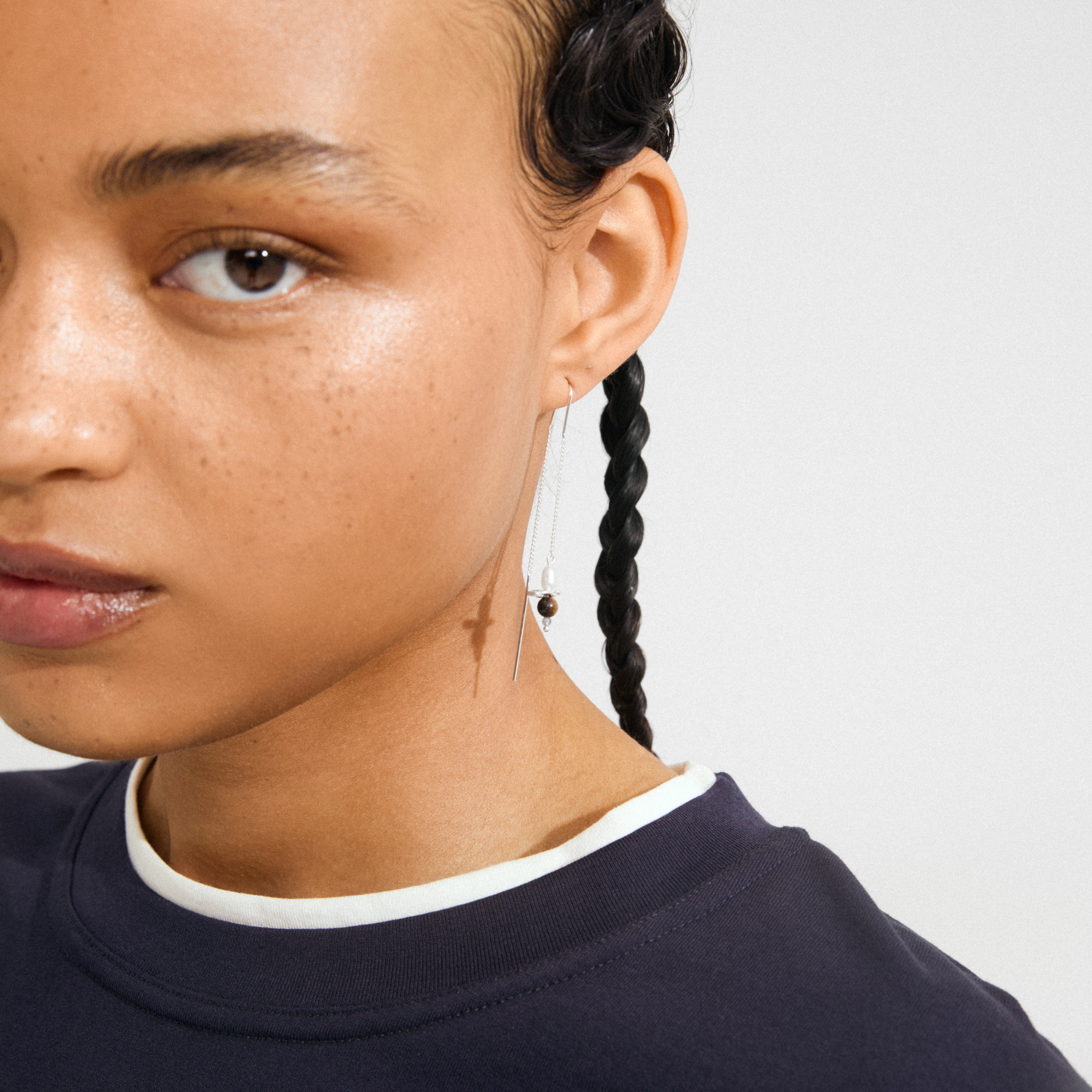 Close-up of a freckled cheek showcasing a silver-plated SEQUOIA chain earring with beads, highlighting its delicate, handcrafted design by Pilgrim.