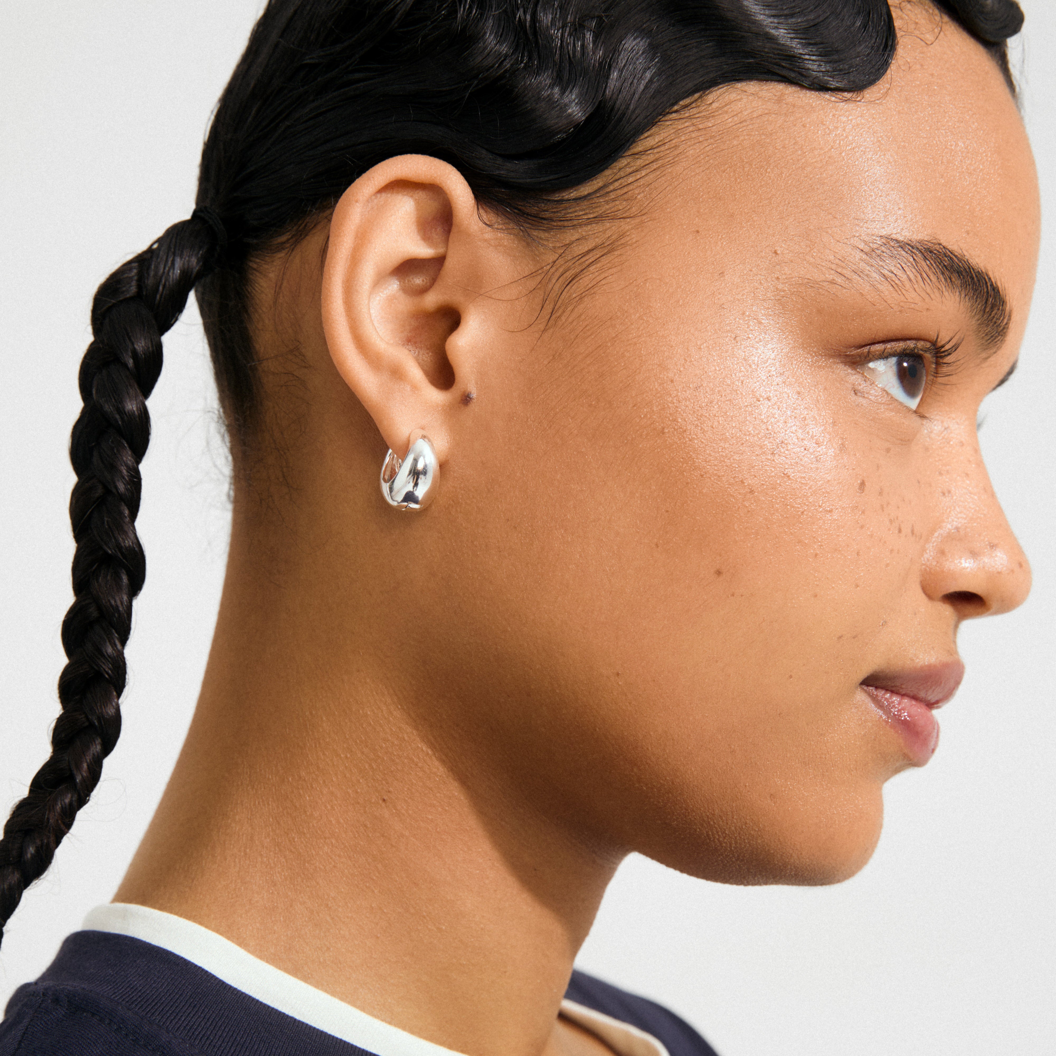 Close-up of a person wearing Pilgrim's BRAXTYN silver-plated chunky hoop earring, showcasing its shiny, smooth dome silhouette and retro-inspired design.
