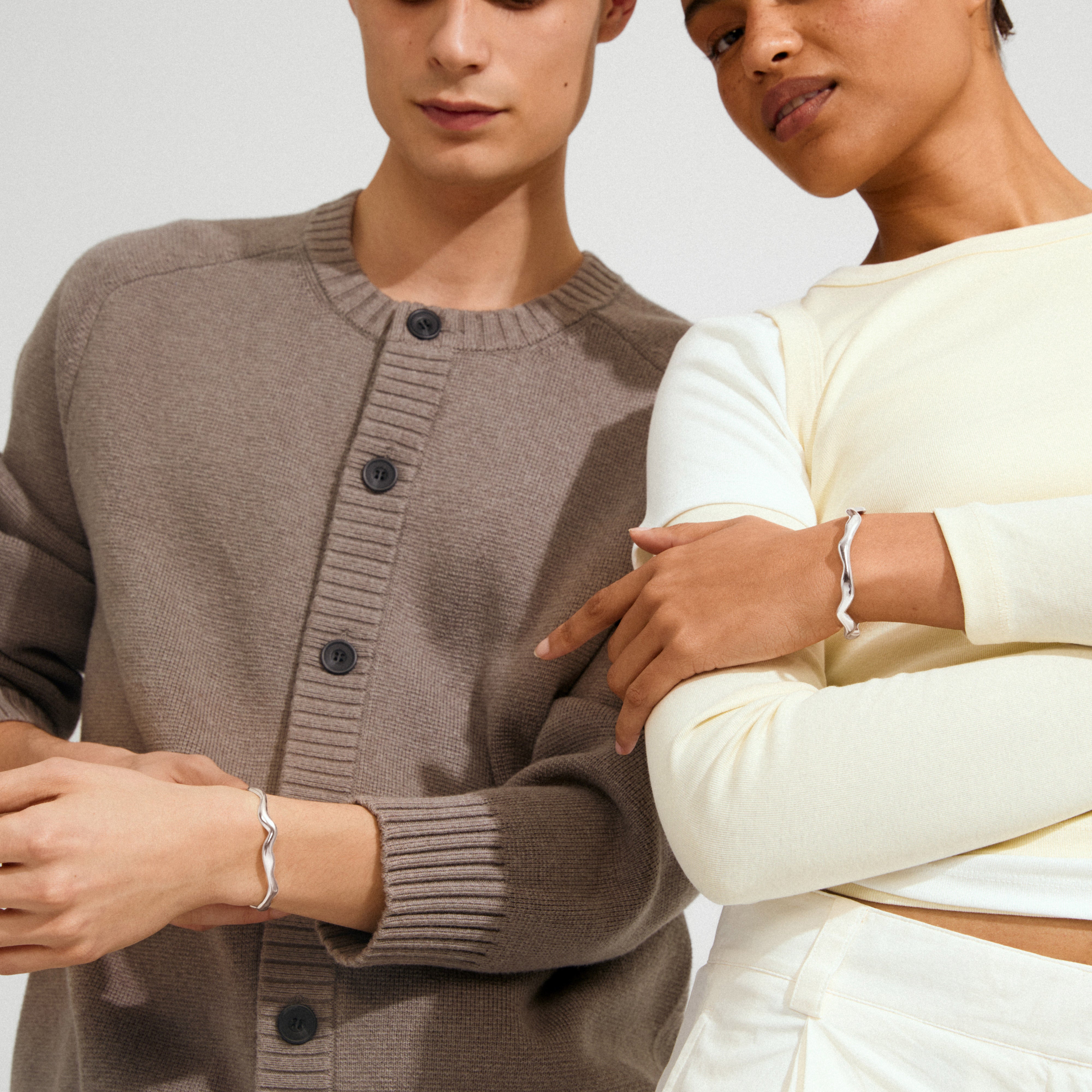 Models display the AIKO bracelet, a silver-plated, wavy bangle, highlighting its minimalist, organic design ideal for stacking or solo wear.
