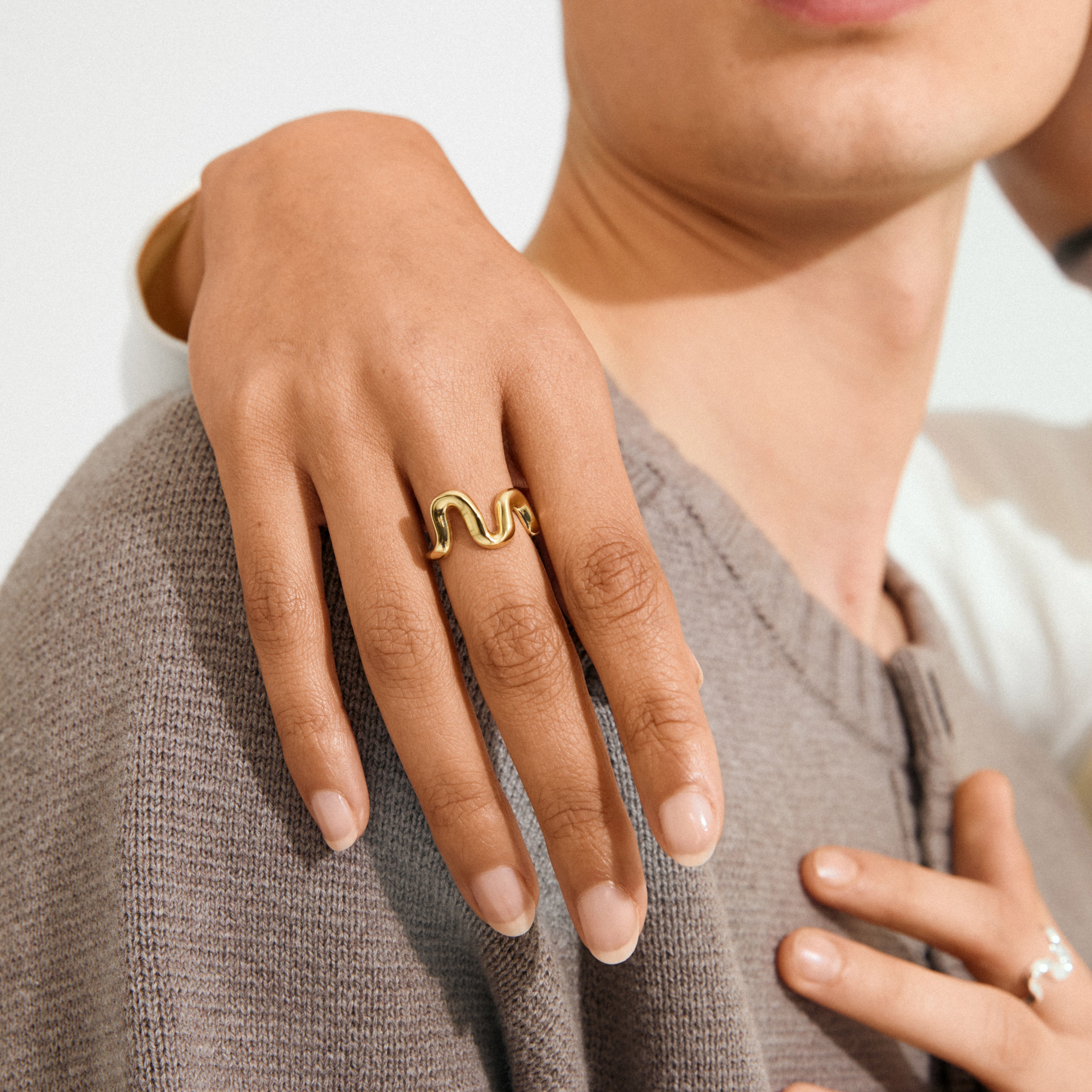 AIKO ring silver-plated showcased with a smooth, wavy design on a hand over a shoulder, highlighting its sculptural elegance and textured knit fabric contrast.