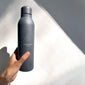 Grey recycled steel thermos bottle, 470 ml, held by hand. Features vacuum insulation and matte finish, ideal for maintaining drink temperatures.