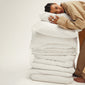 A woman hugging a stack of white pillows, wearing the PILGRIM PJ set XS/S, showcasing its relaxed, oversized fit and cozy style.