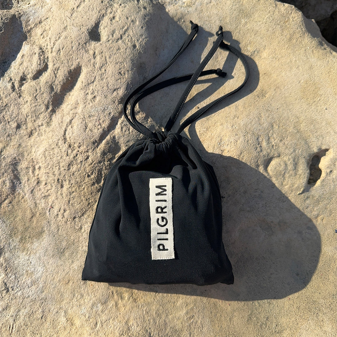 Black bikini in XS/S with triangle top and high-cut bottoms, featuring earthy chunky beads and side ties, packed in a Pilgrim logo pouch.