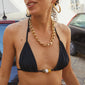 Close-up of a woman wearing a black bikini top with earthy-toned chunky beads and a gold necklace, showcasing Pilgrim's boho chic swimwear style.