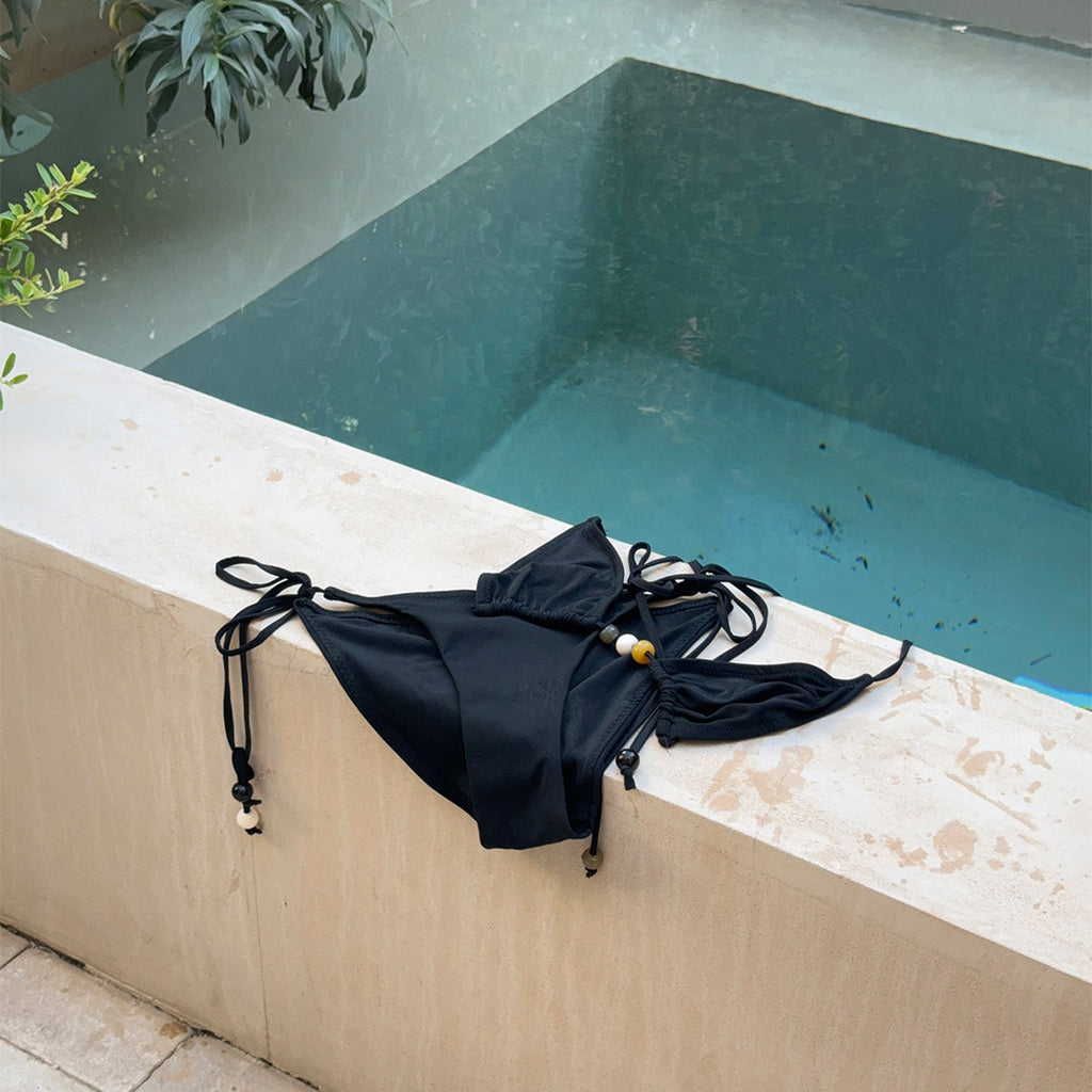 Black bikini, size M/L, featuring a triangle top with chunky beads, high-cut bottoms, and side ties, embodying a boho chic beach style.