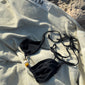 Black bikini with triangle top, earthy-tone beads, high-cut bottoms, side ties, and decorative straps, packed in a black drawstring pouch labeled 'Pilgrim', size M/L.