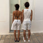 Man wearing Pilgrim’s off-white Wherever you go shorts, showcasing oversized fit and button detail, paired with a white tank top, embodying casual style.