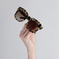 Hand holding Dael sunglasses with a chunky retro butterfly frame, showcasing Pilgrim's trendy design and UVA/UVB protection.