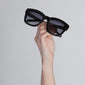 Dael Black sunglasses with chunky butterfly-shaped frame, held in hand, offering UVA/UVB protection and polarized lenses for a trendy, retro-inspired look.