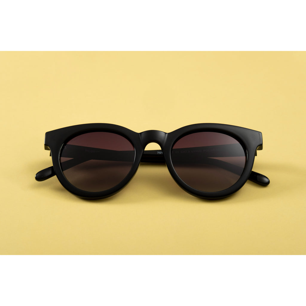 Sunglasses: Meriel: Black - Classic round sunglasses with black frames, brown lenses, and metal temple detail, offering stylish sun protection.