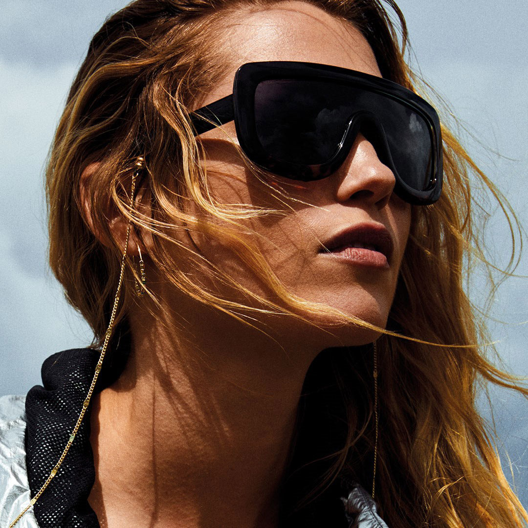 Woman wearing sunglasses with a gold-plated CAT chain from Pilgrim, featuring a simple yet glamorous pattern, perfectly complementing Pilgrim eyewear.