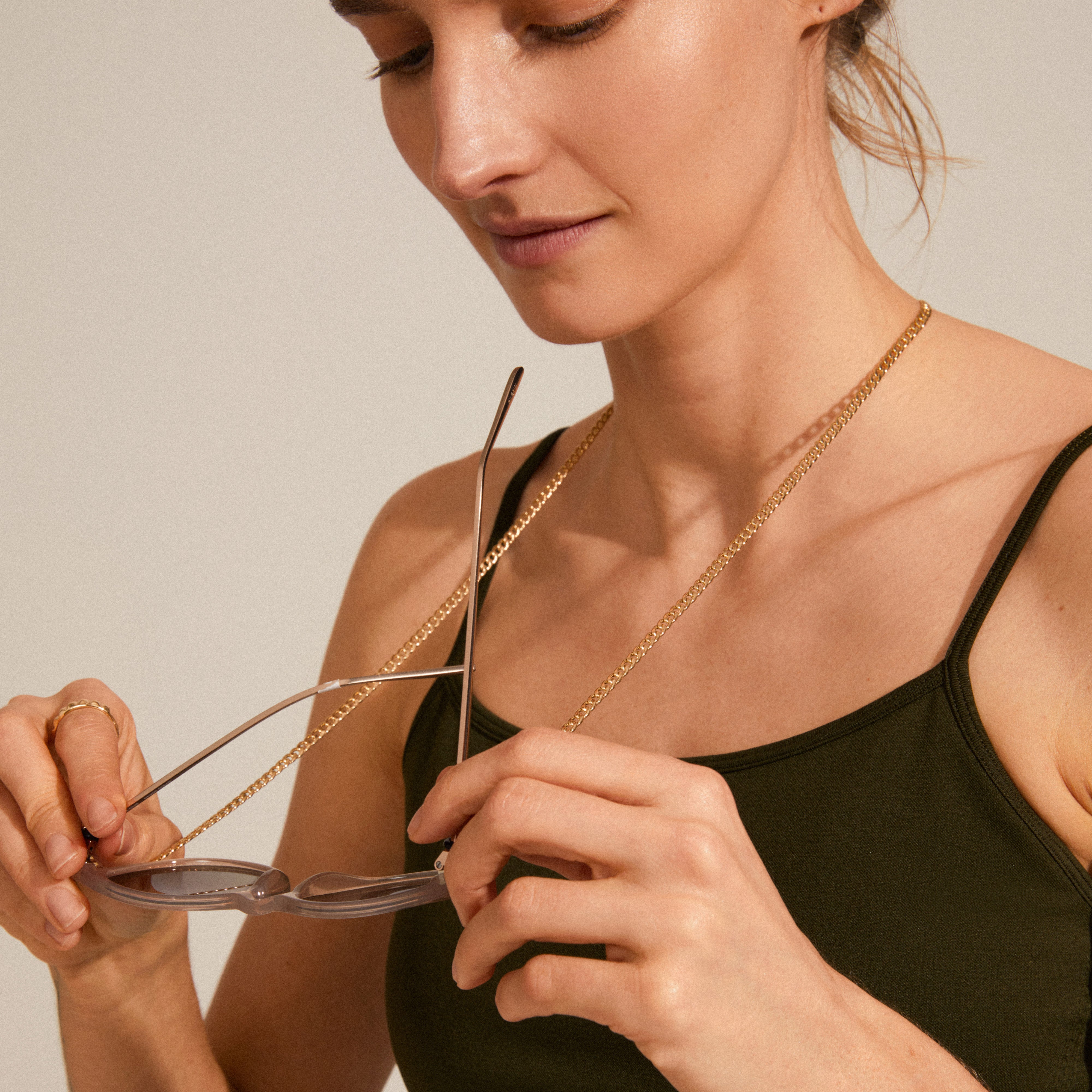 Woman elegantly holding AJA curb chain for sunglasses, showcasing gold-plated, 85 cm curb chain with adjustable loops, enhancing sunglasses with stylish, trendy flair.