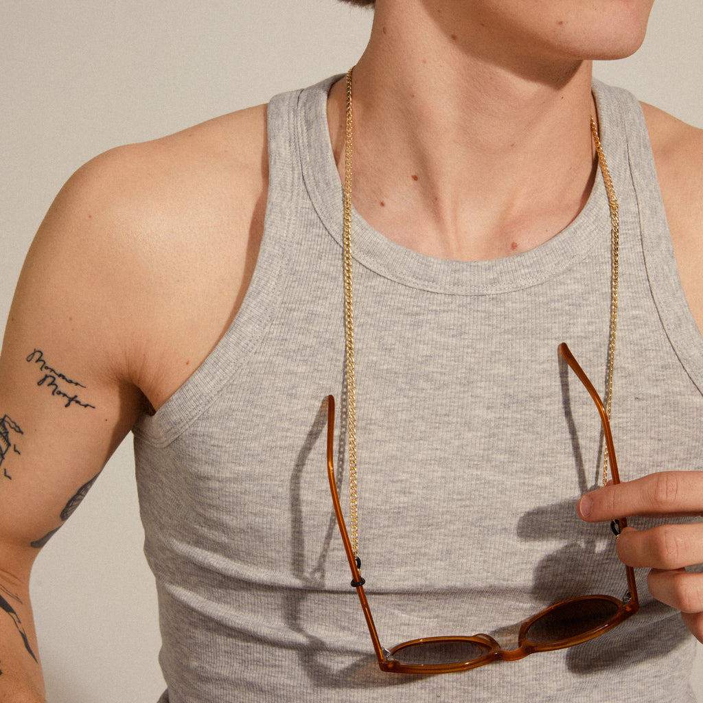Person wearing a grey tank top and gold chain, holding sunglasses with the AJA curb chain for sunglasses gold-plated attached.