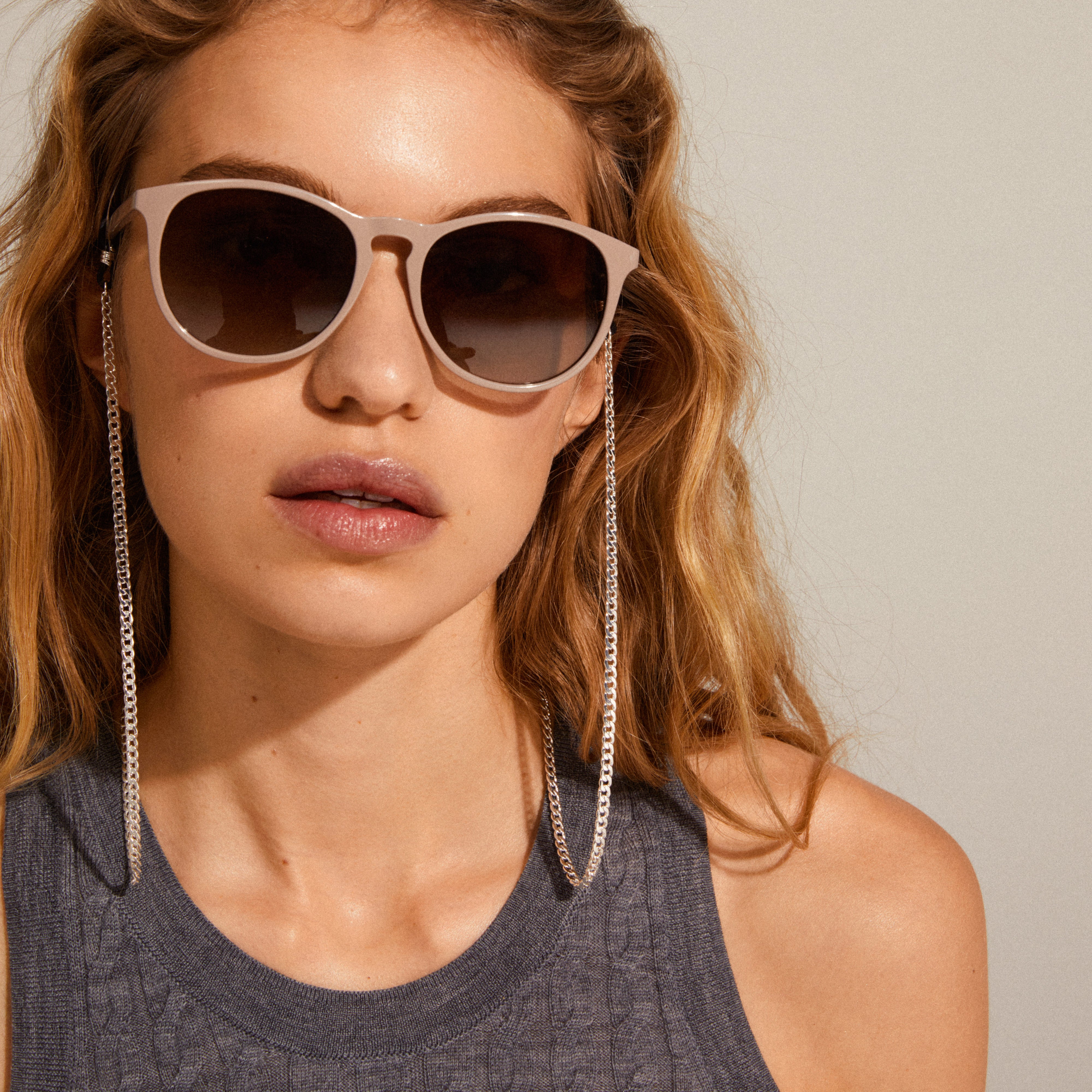 A woman wearing sunglasses with the AJA curb chain for sunglasses silver-plated, enhancing the look with a stylish, silver-plated accessory.