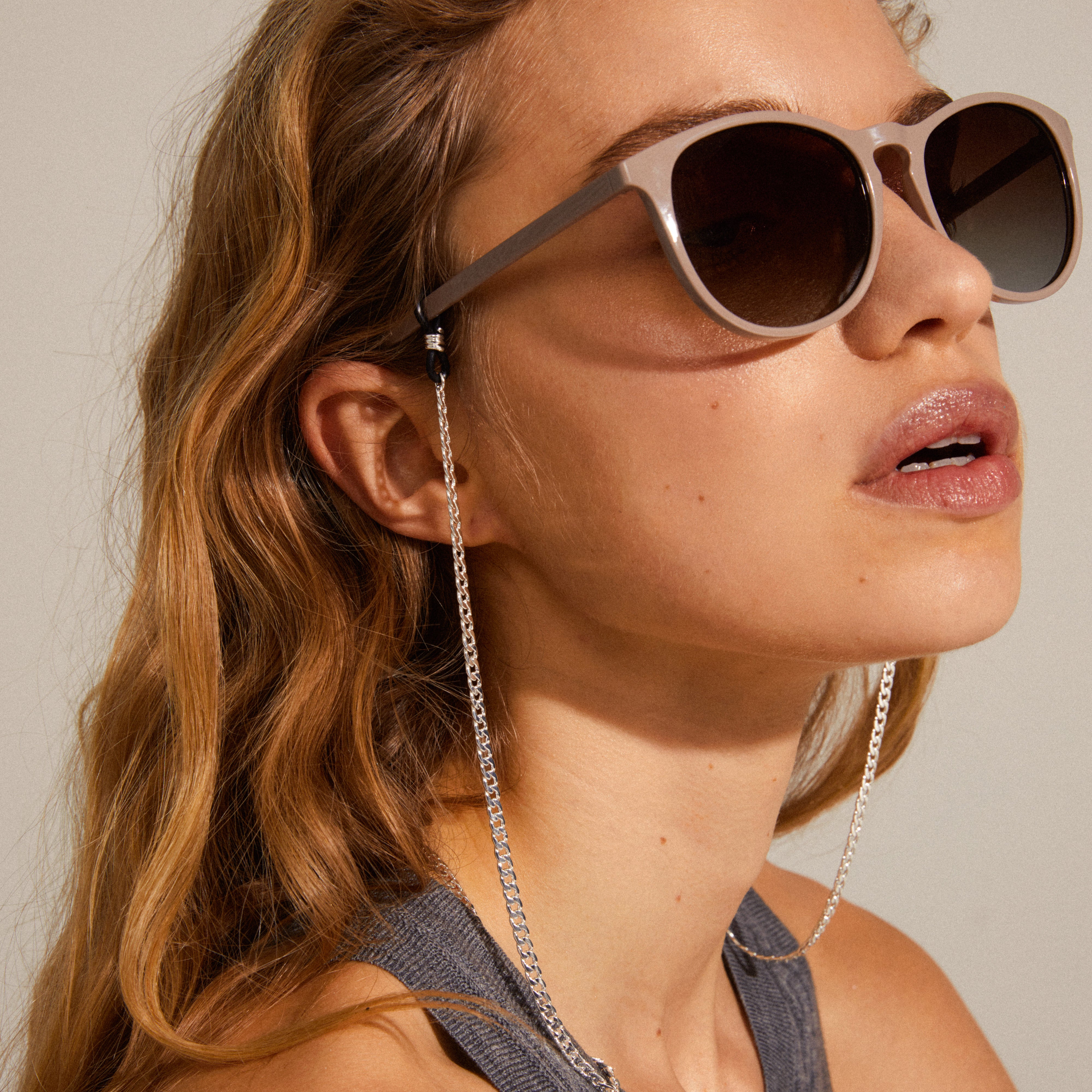Woman wearing sunglasses with AJA silver-plated curb chain attached, showcasing a stylish accessory designed for sunglasses, enhancing both function and fashion.