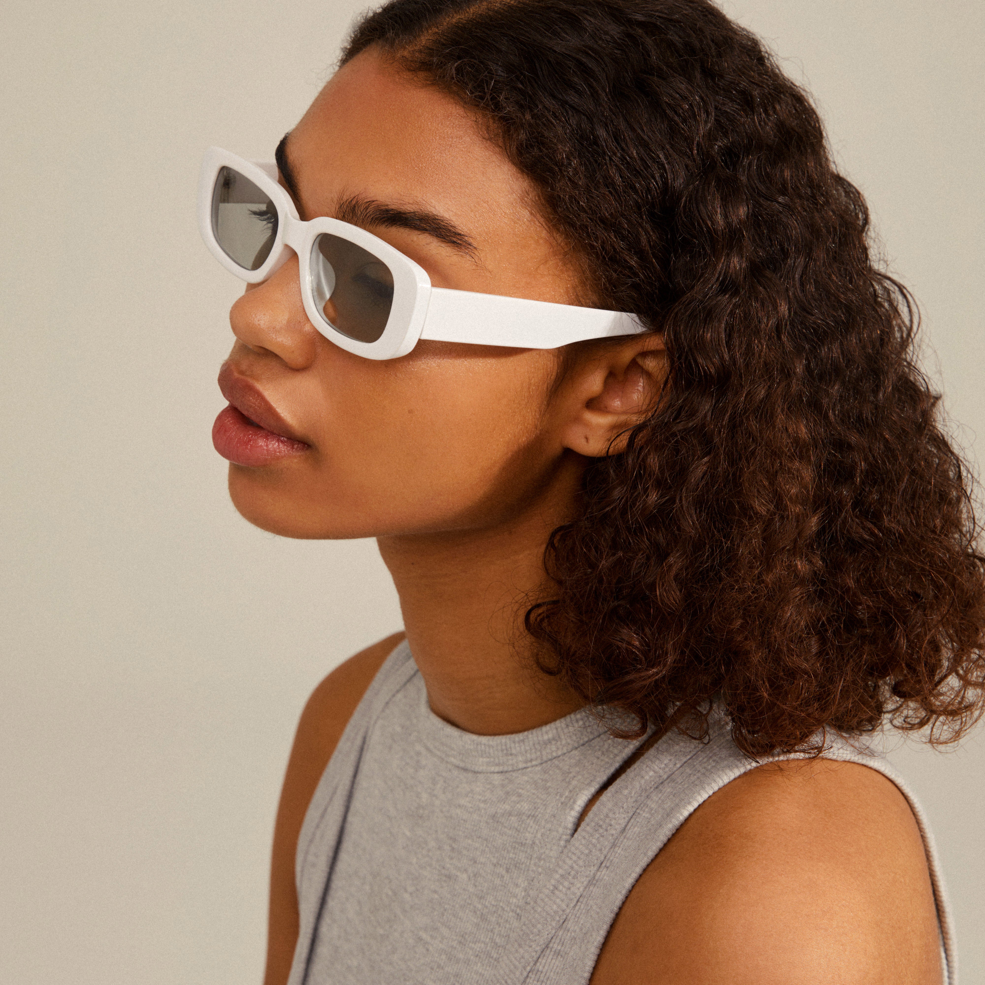 Woman wearing YANSEL white sunglasses, featuring a chunky, vintage-inspired square design. Perfect for trendsetters, made from recycled plastic with UVA/UVB protection.