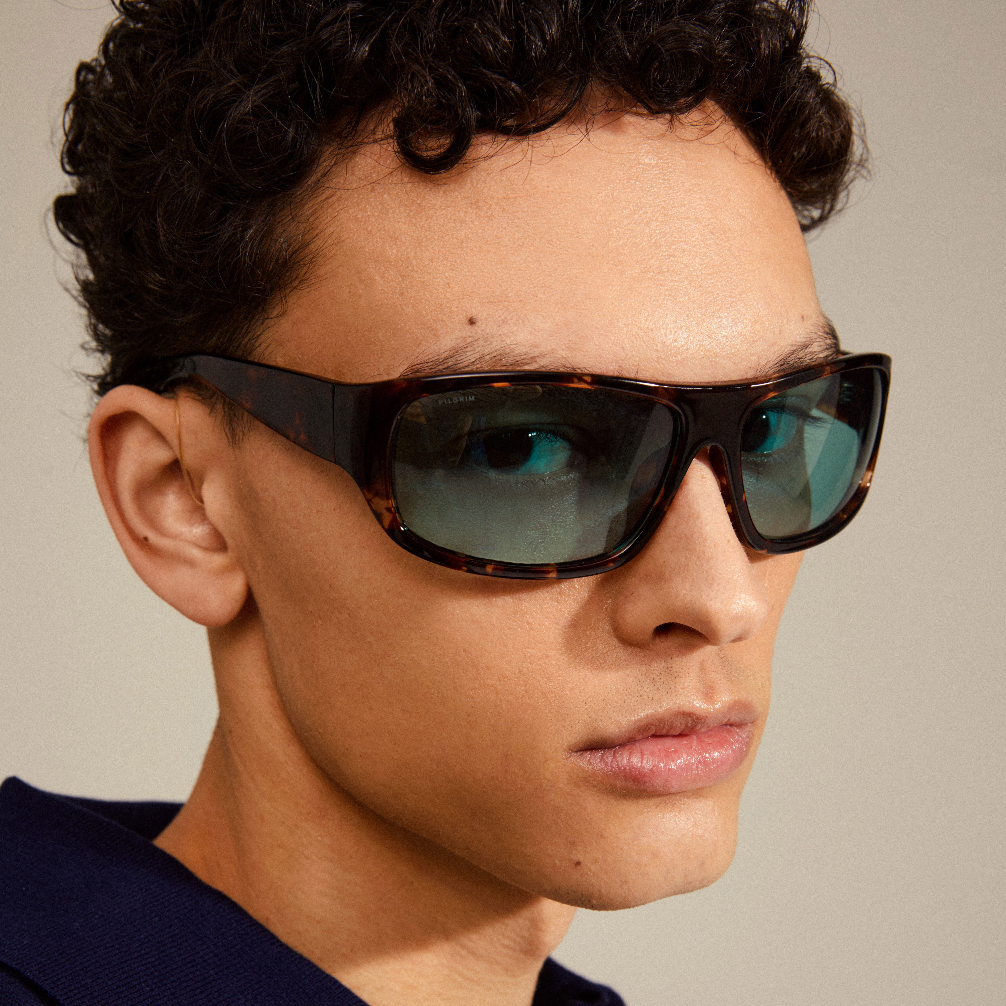 Man wearing GERTRUD sunglasses by Pilgrim, featuring tortoise brown frames with trendy light blue lenses, offering UVA/UVB protection, styled with confidence and edge.