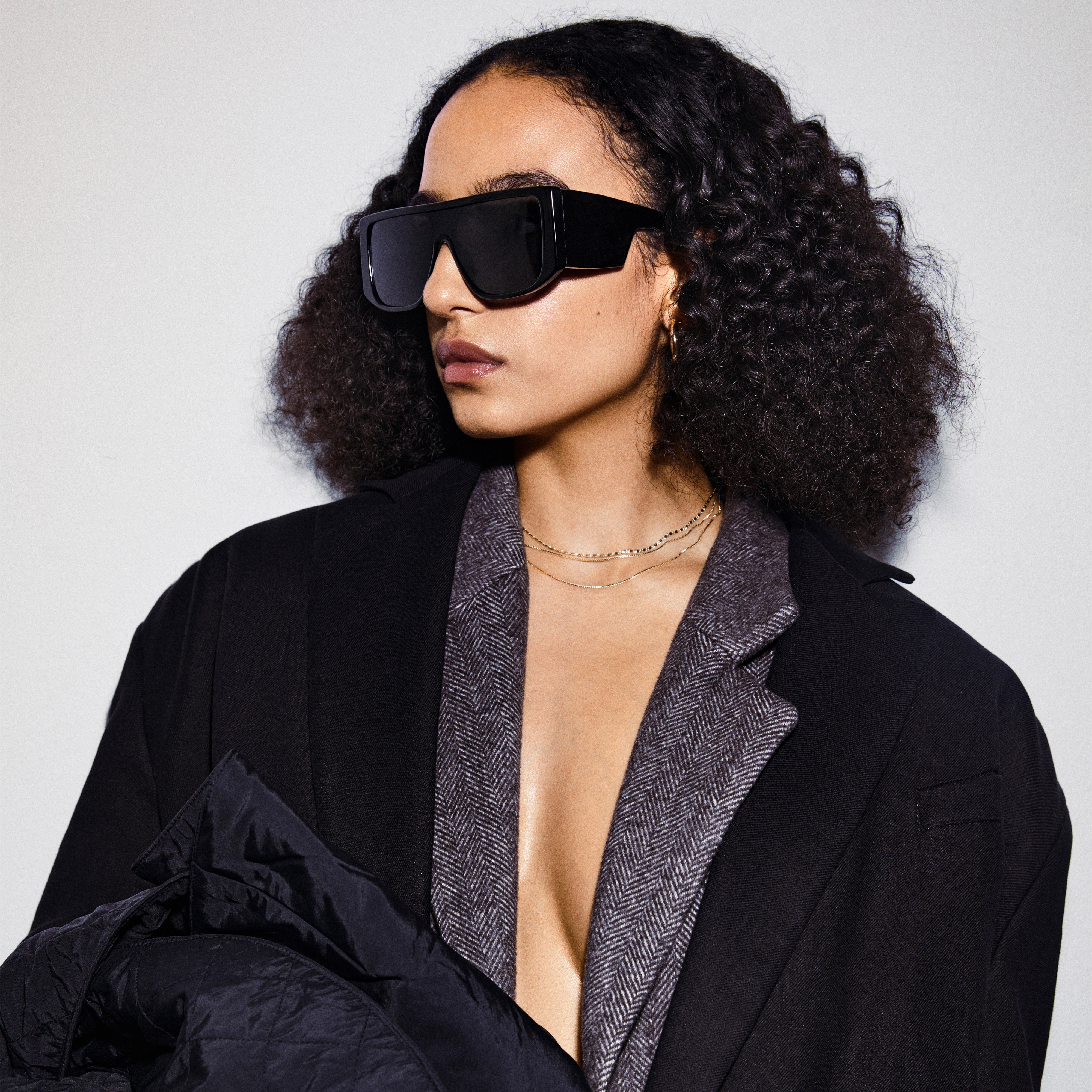 Woman wearing JOHARI sunglasses with oversized black frames and dark lenses, showcasing trendy L.A. style; part of Pilgrim's sustainable eyewear collection.