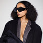Woman wearing JOHARI sunglasses with oversized black frames and dark lenses, showcasing trendy L.A. style; part of Pilgrim's sustainable eyewear collection.