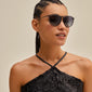 Woman wearing VANILLE sunglasses in grey/gold, showcasing their stylish design with golden temples, perfect for any occasion. Part of Pilgrim's chic accessory collection.