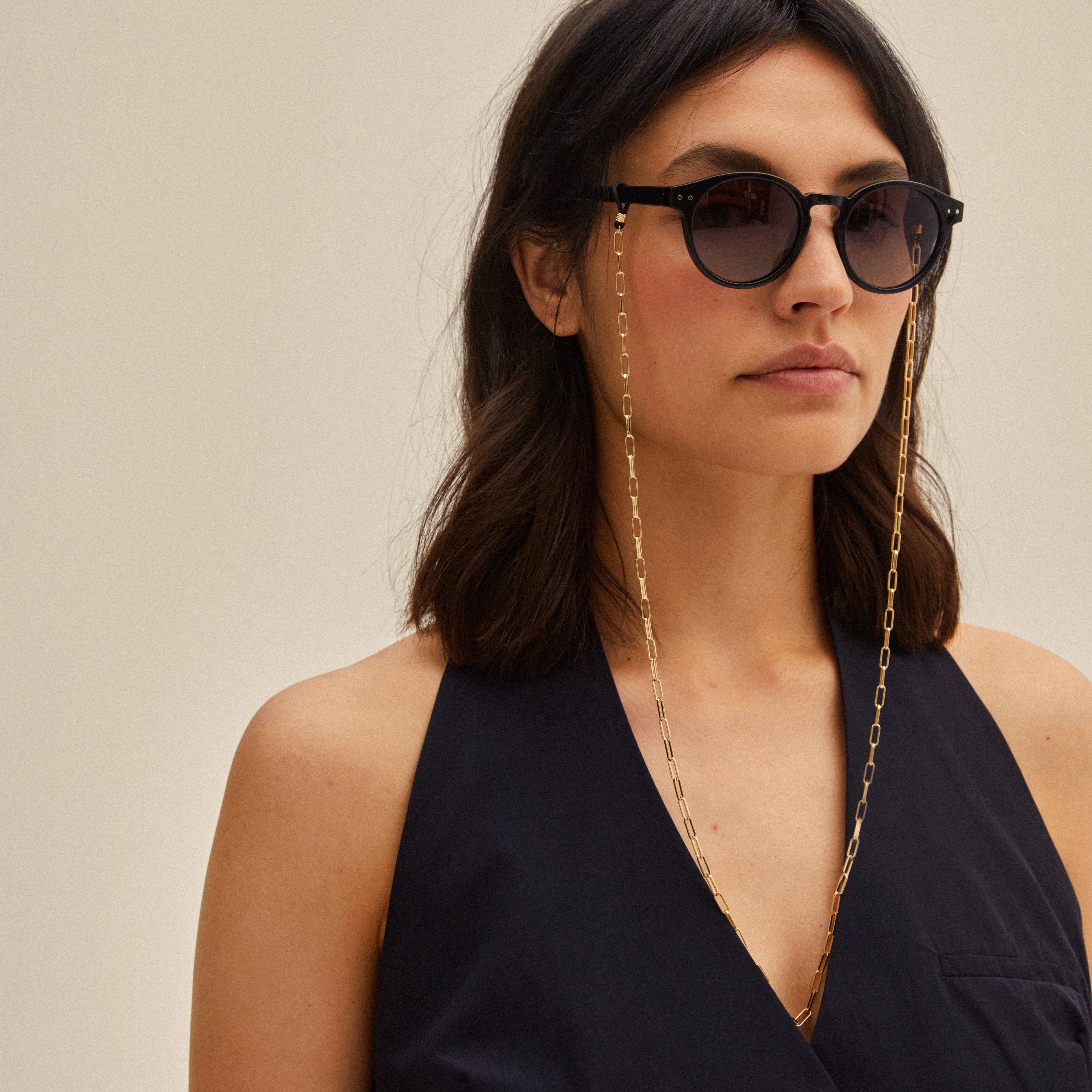 Woman wearing sunglasses with the PAOLA gold-plated chain for sunglasses, featuring a delicate cable-chain style, adding elegance to her look.