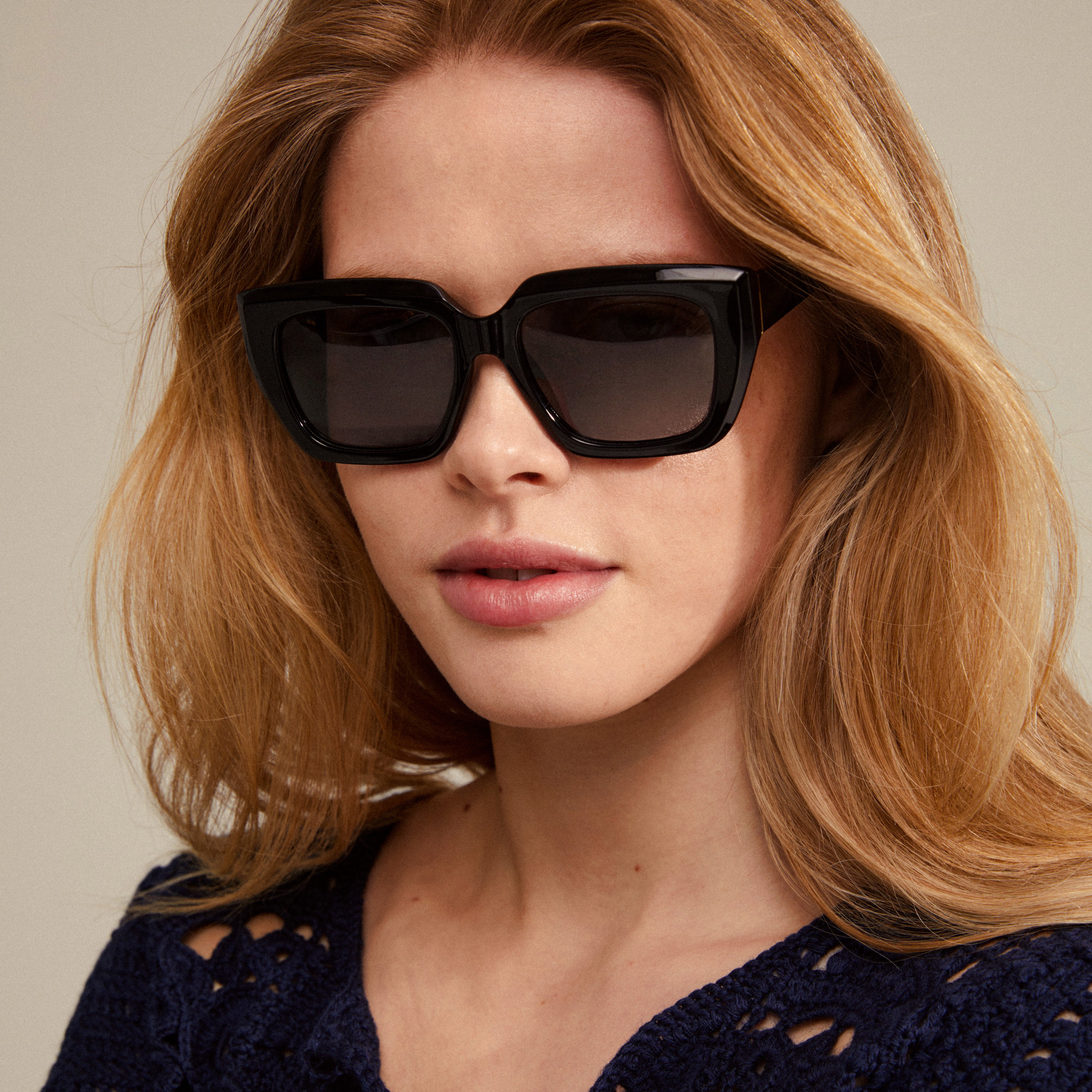 Woman wearing JOGLI sunglasses black/gold with oversized design and gold details, showcasing Pilgrim's blend of trend and sustainability.