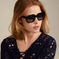 Jogli sunglasses in black/gold with oversized design, sharp frames, and golden hinge details, worn by a woman, reflecting Pilgrim's trendy and inclusive style.