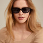 NELLA sunglasses in black/gold, worn by a woman, showcasing trendy eyewear with recycled acetate frames, perfect for summer adventures.