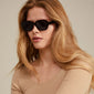 NELLA sunglasses black/gold: A woman with long hair wears stylish sunglasses featuring black frames, perfect for summer adventures and fashionable outings.