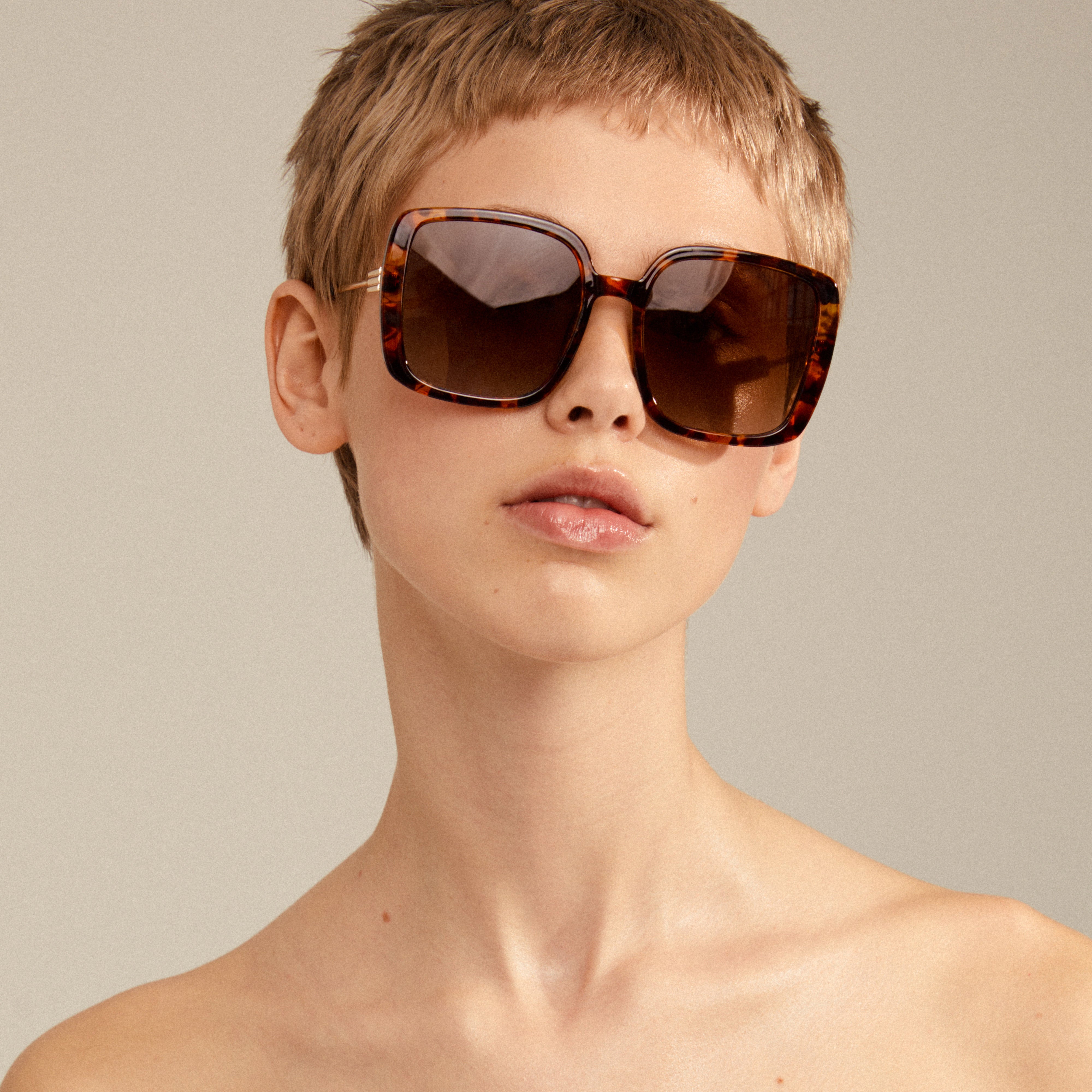 Woman with short hair wearing Aliet sunglasses, featuring oversized square frames and dark green lenses, embodying a retro-vibe from Pilgrim's collection.