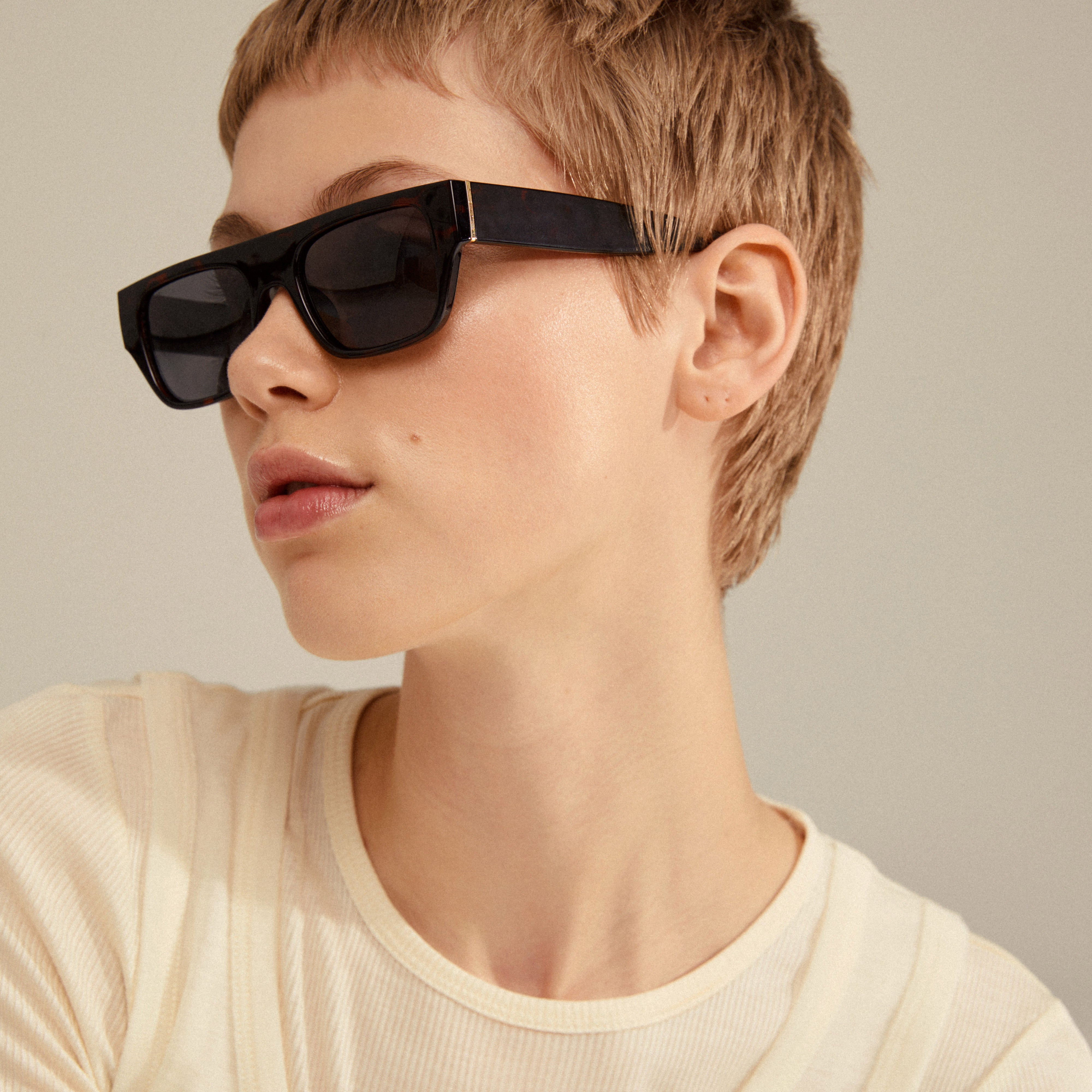 ENIEL sunglasses in tortoise brown/gold, featuring a classic design with dark lenses, worn by a woman with short hair, embodying a stylish summer look.