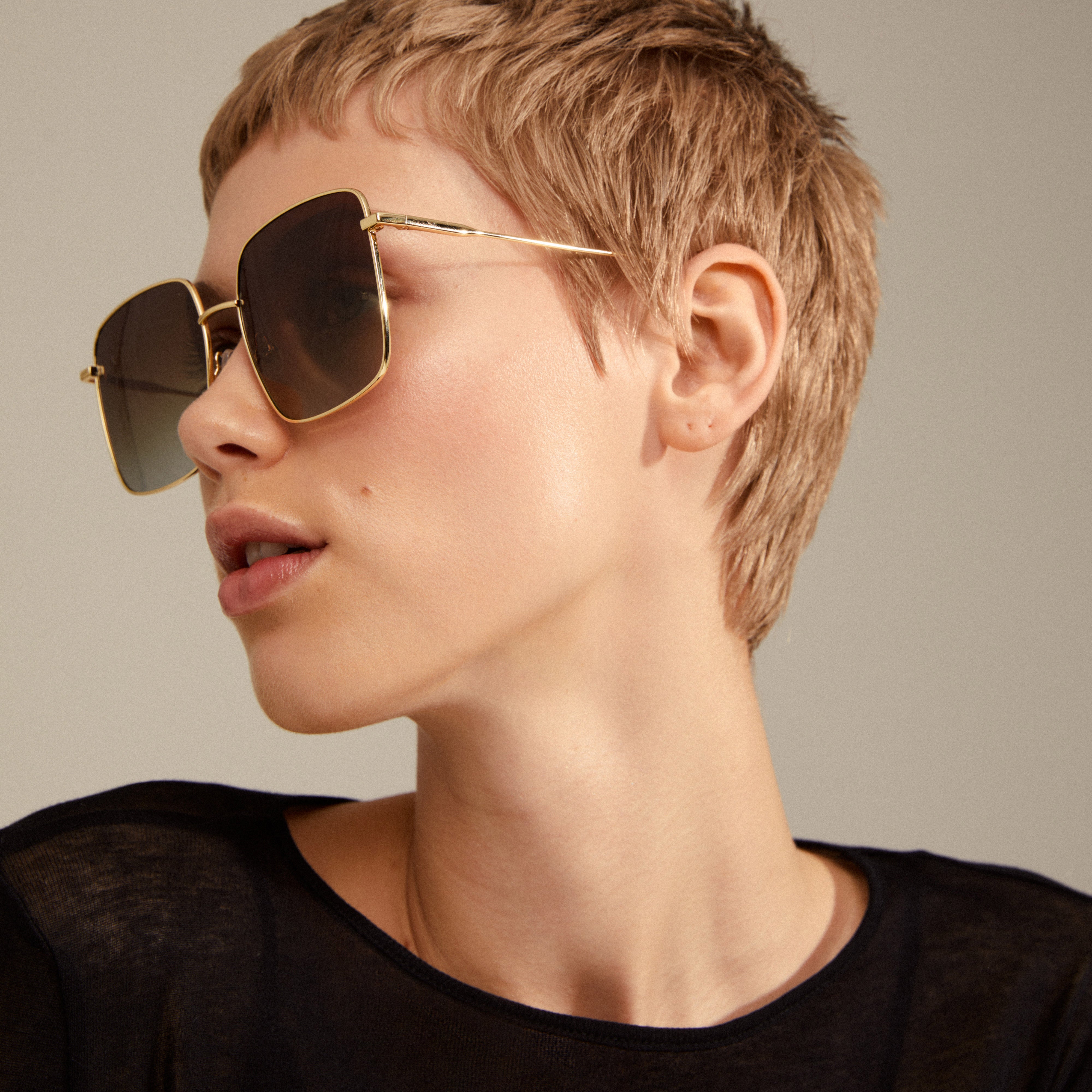 Woman wearing JONAN sunglasses with oversized brown lenses and thin gold temples, capturing a vintage 70s summer vibe. Ideal for festivals and holidays.