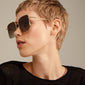 Woman wearing JONAN sunglasses with oversized brown lenses and thin gold temples, capturing a vintage 70s summer vibe. Ideal for festivals and holidays.