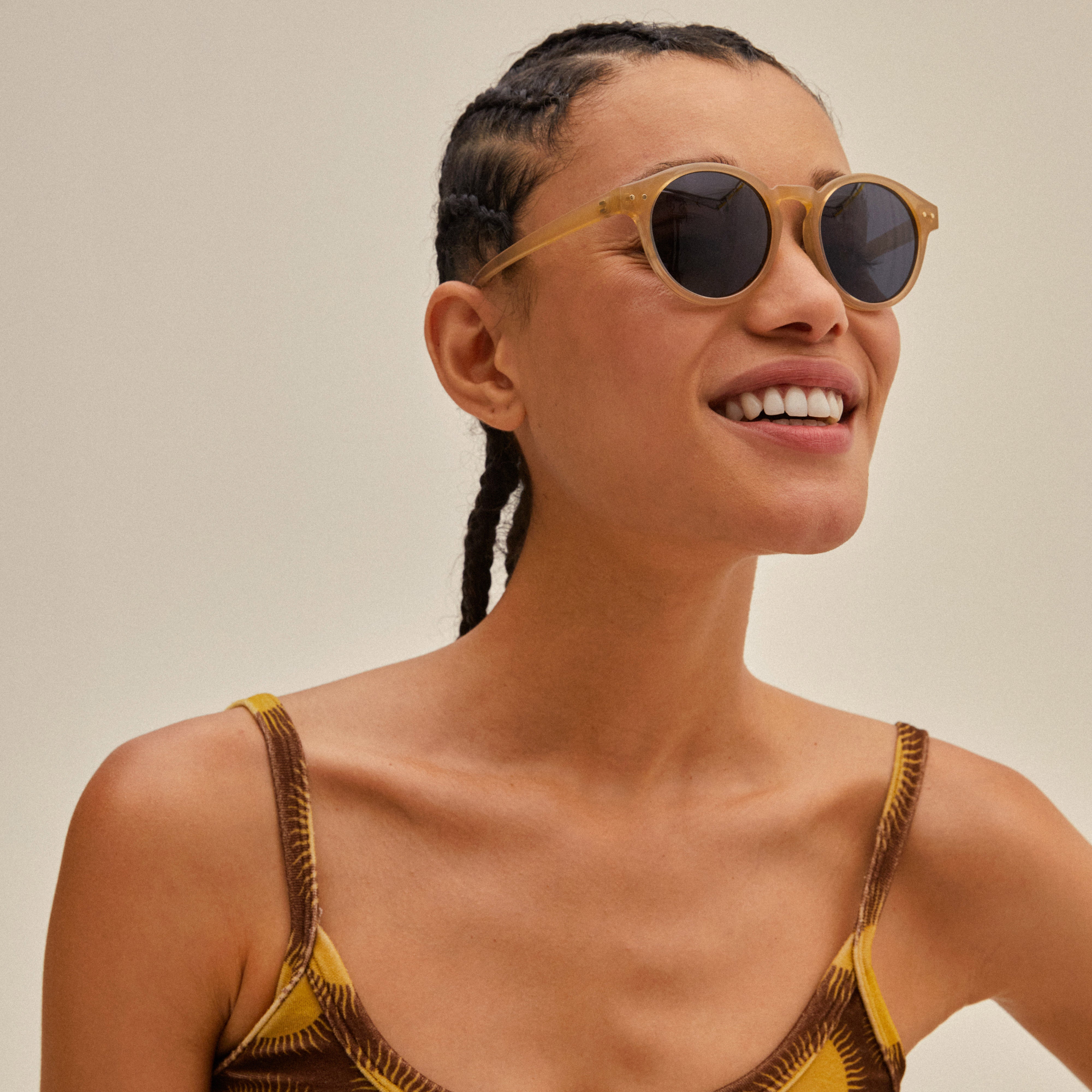 Woman smiling in KYRIE sunglasses, light brown/gold by Pilgrim, showcasing classic shape and Nordic sophistication with smoke-colored lenses.
