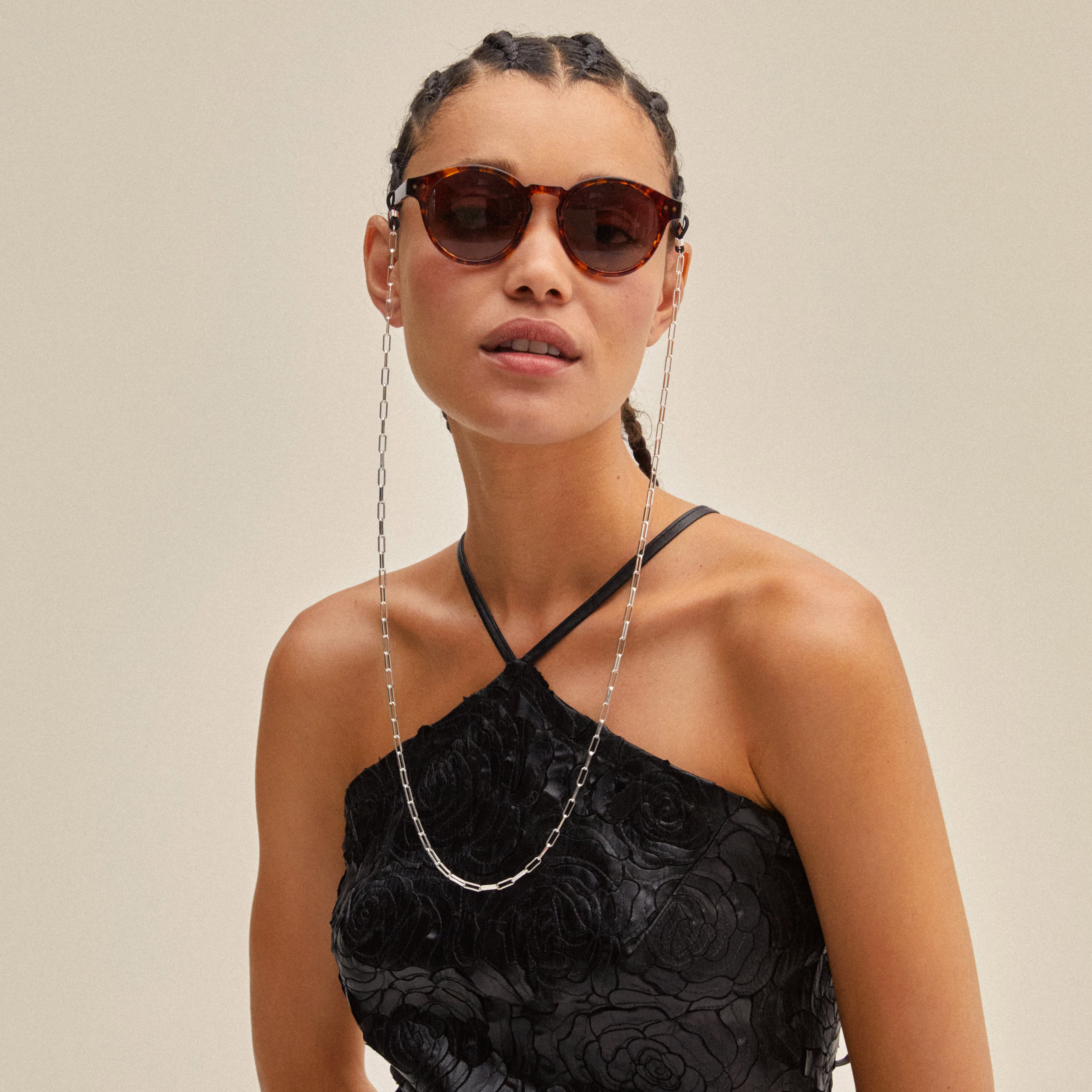 Woman in black dress wearing sunglasses with PAOLA silver-plated chain attached, featuring delicate cable-chain design, enhancing her stylish and trendy look.