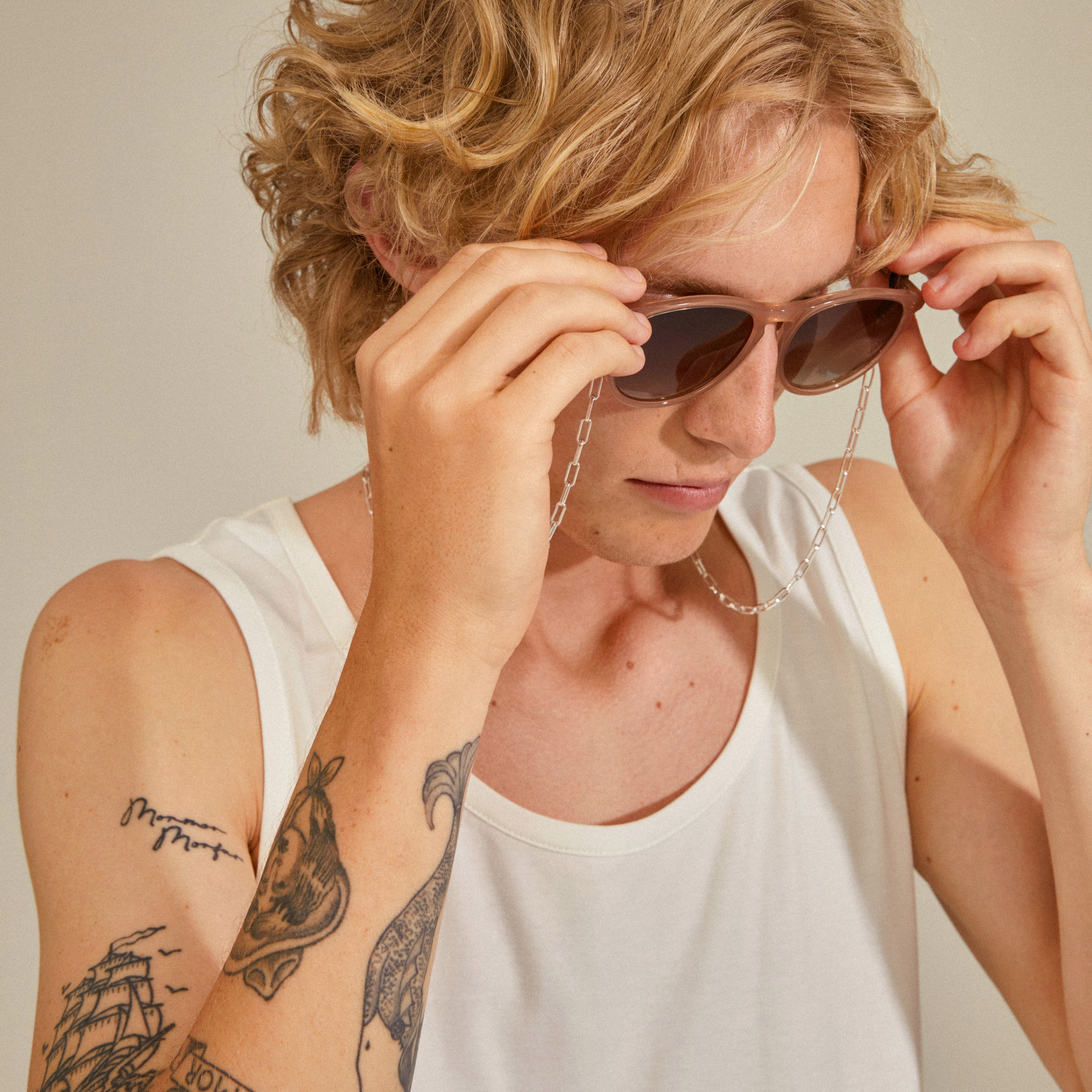 Close-up of person wearing PAOLA silver-plated chain for sunglasses, showcasing its stylish cable-chain design, attached to sunglasses with black rubber loops.