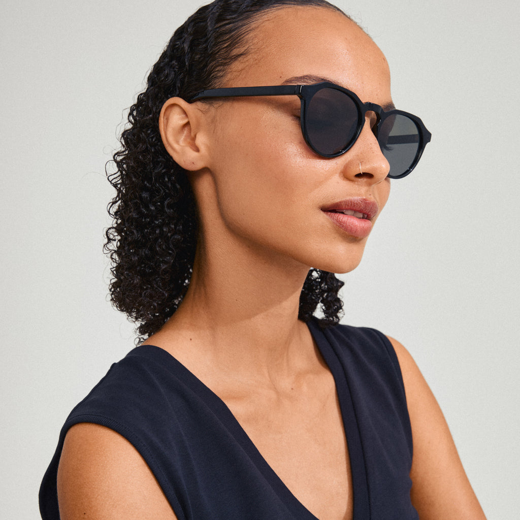 Woman wearing ALEJANDRA sunglasses black by Pilgrim, showcasing a modern round frame with angular details, embodying a trendy and confident style.